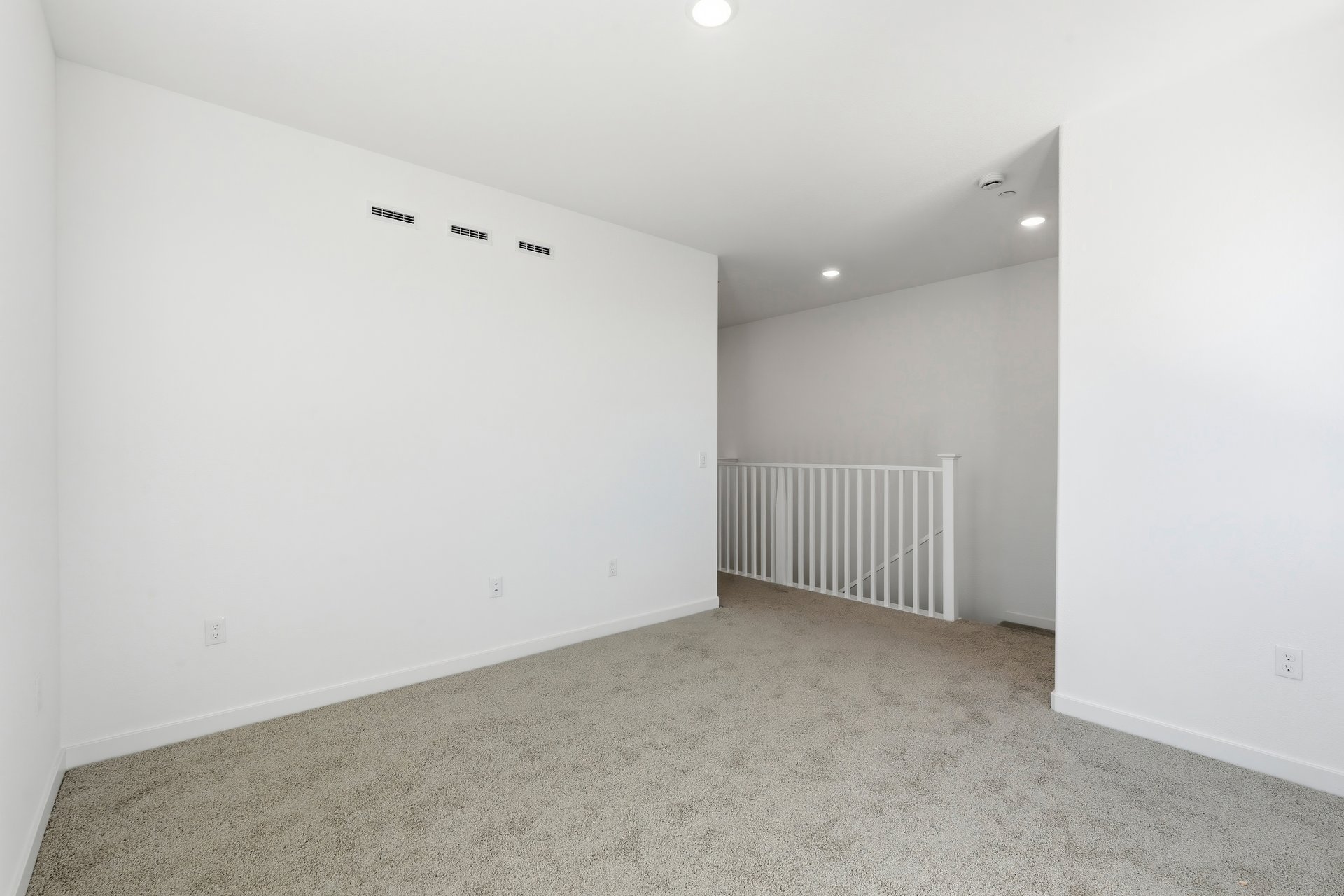 loft with gray carpet, white walls, and view of white staircase railing