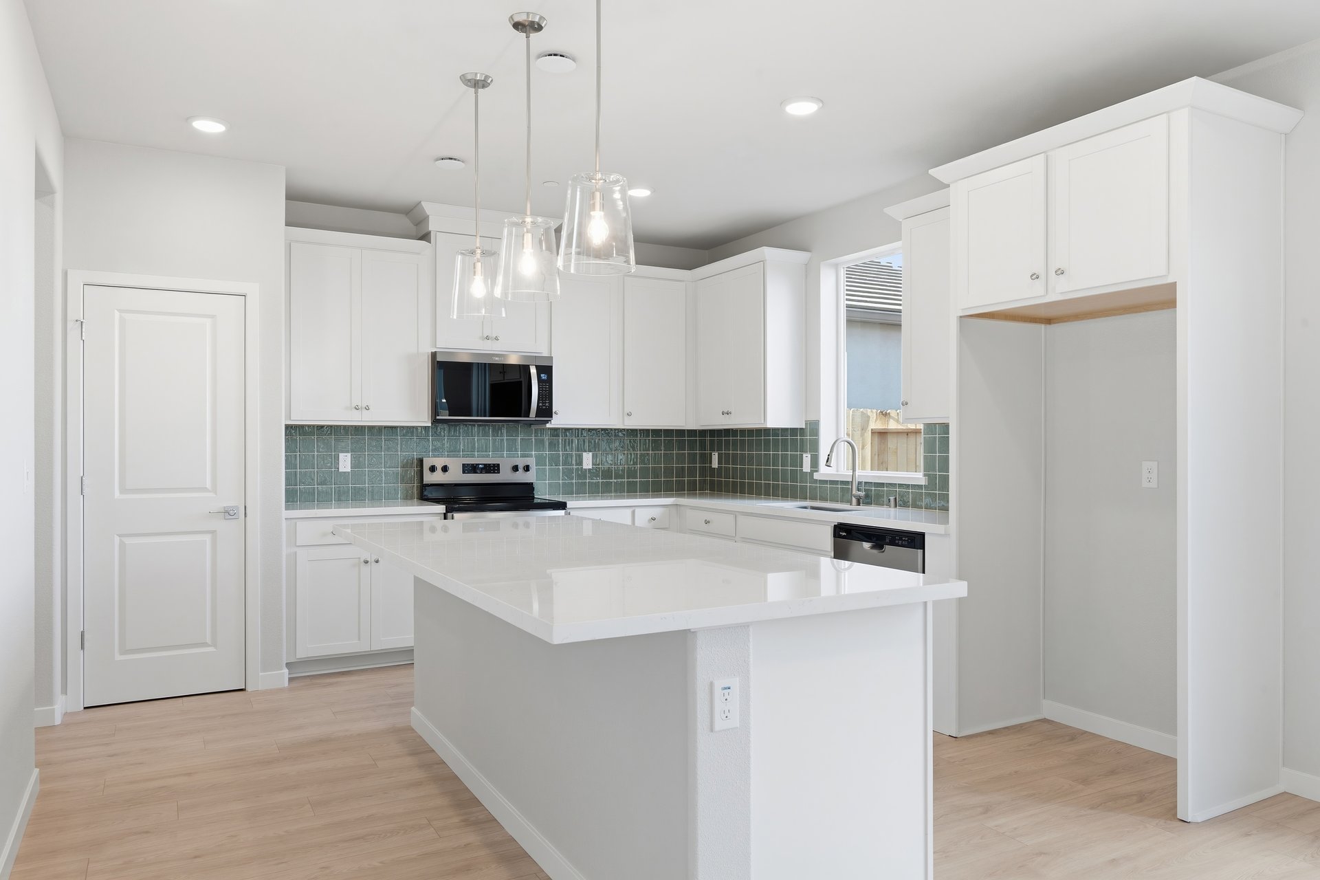 kitchen with white cabinets, white quartz counters, green tile backsplash, island, and window above sink