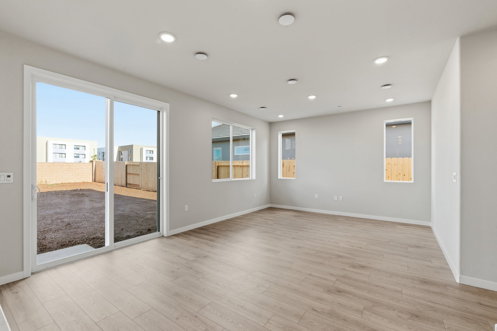 great room with light wood floors, three windows, recessed ceiling lights, and sliding glass door to backyard