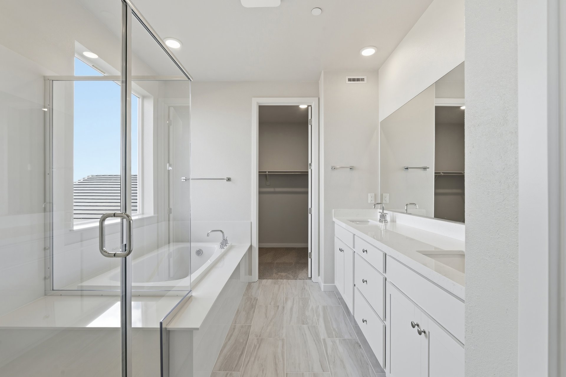 bathroom with white cabinets, white counters, two sinks, walk-in shower, and window above tub
