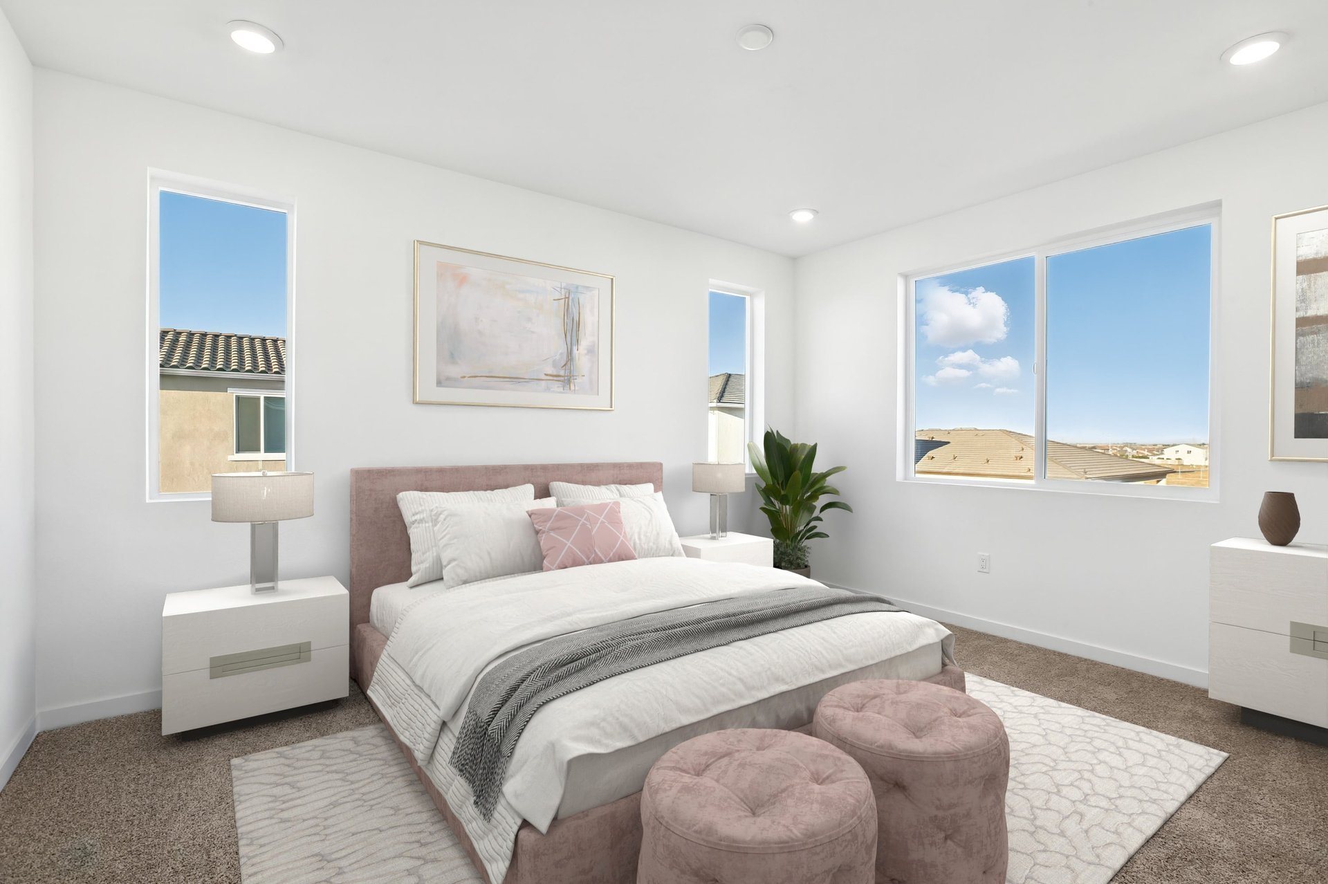 bedroom with tan carpet, pink upholstered bed and ottomans, white dresser & nightstands, and three windows