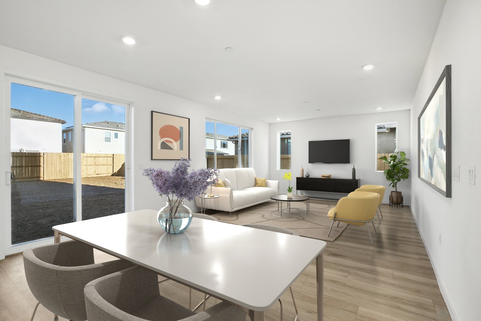 great room with wood floors, white dining table with four tan chairs, white sofa, two yellow accent chairs, and multiple windows