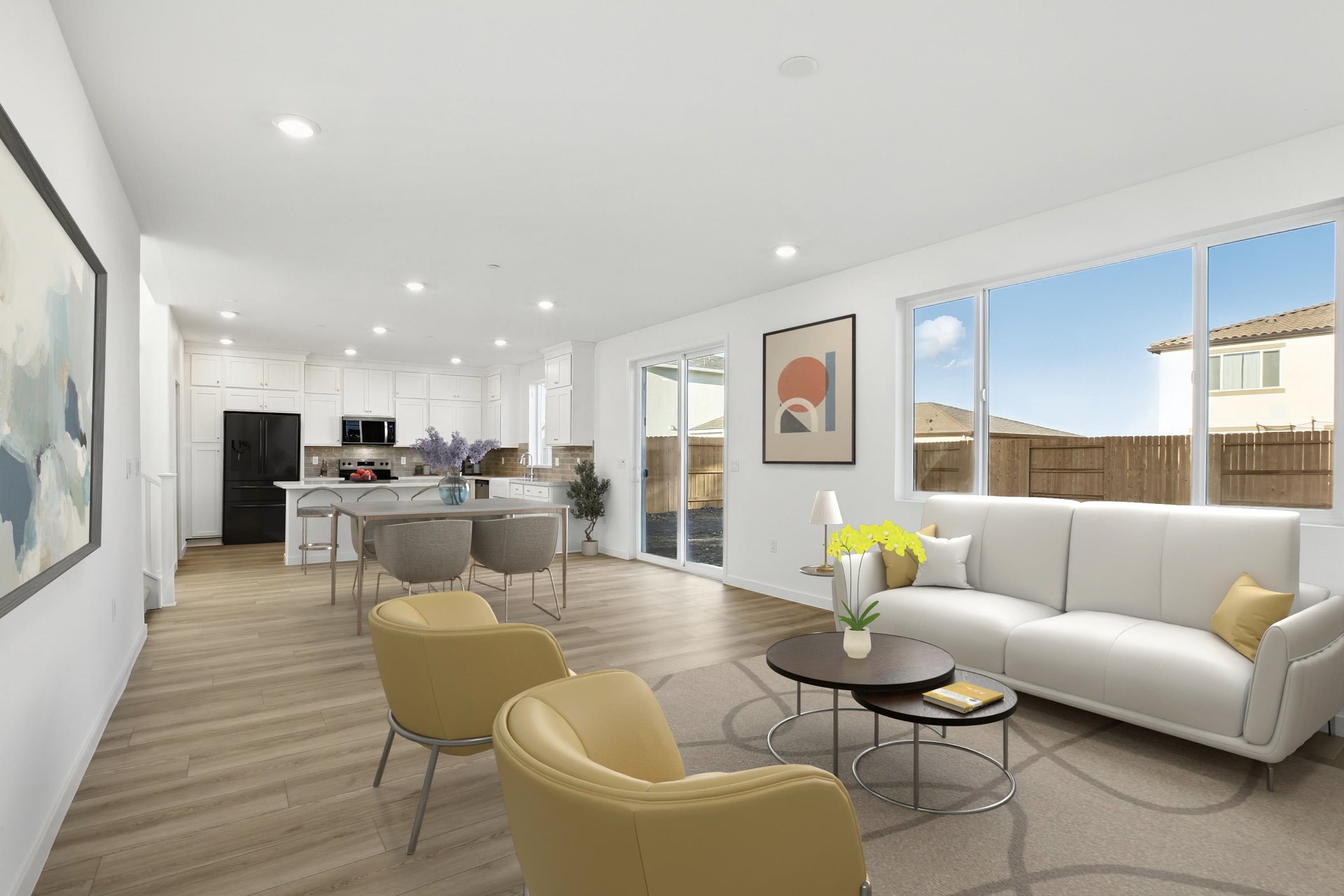 great room with wood floors, large window above white sofa, two yellow accent chairs, modern wall art, and sliding glass door