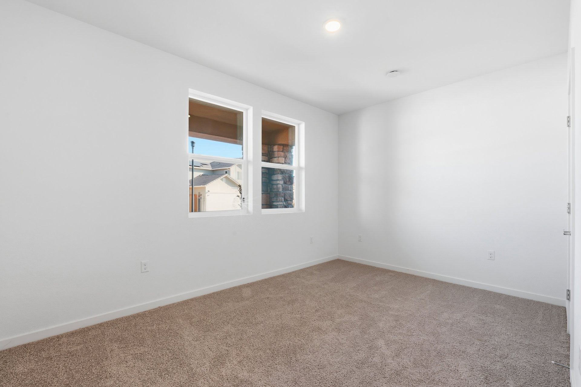 bedroom with tan carpet, white walls, and two windows looking out to front porch