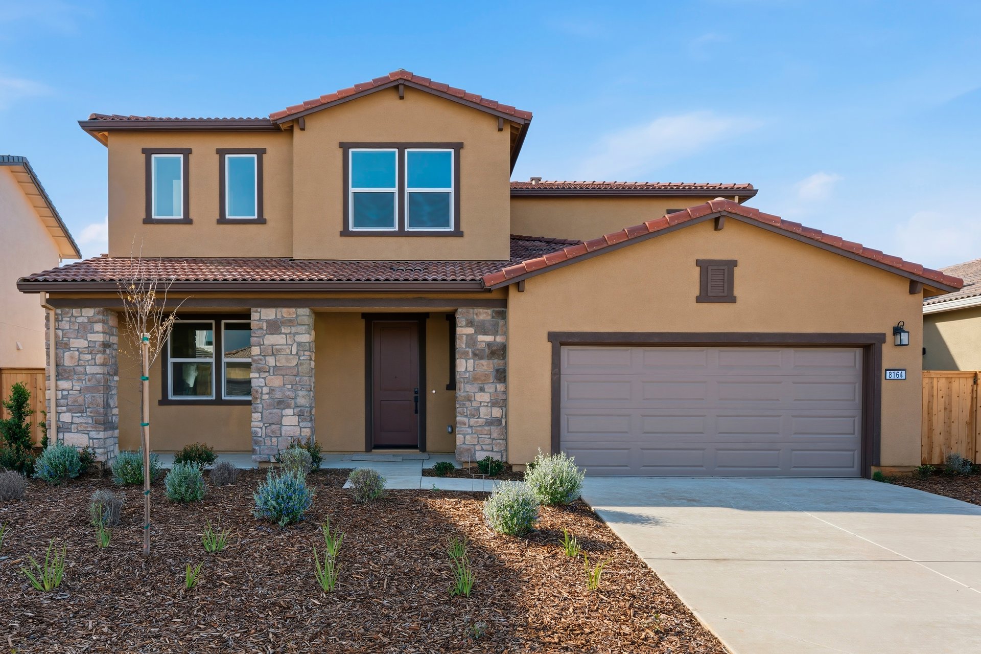 front exterior of two-story spanish style home with terracotta tile roof, brown front door, and covered porch