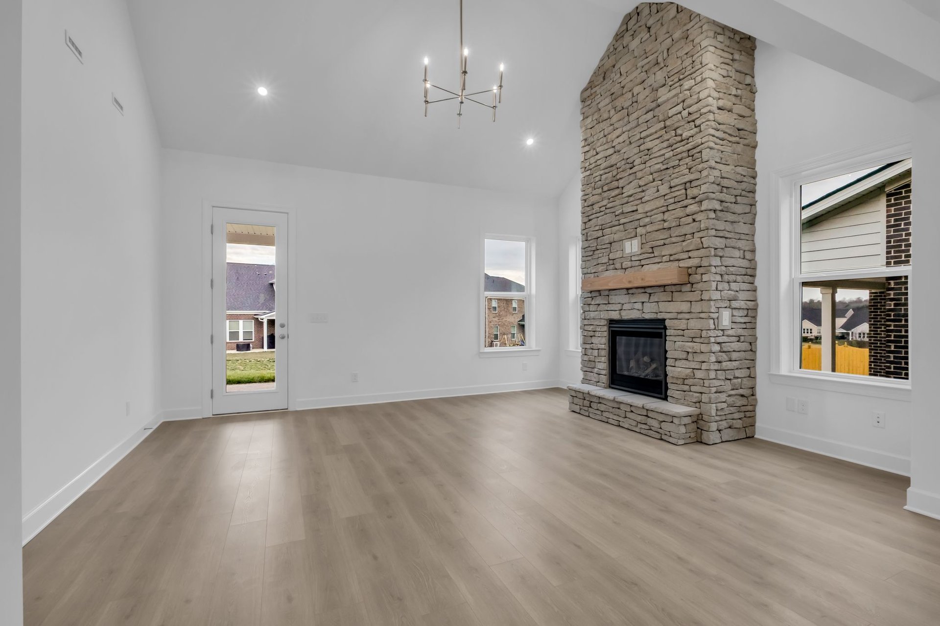 great room with wood floors, vaulted ceilings, and a stone fireplace