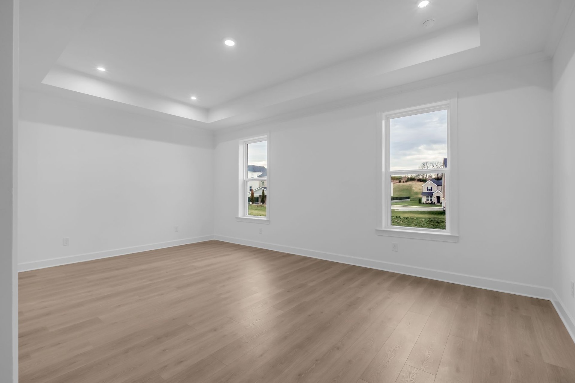 primary bedroom with wood floors and a tray ceiling