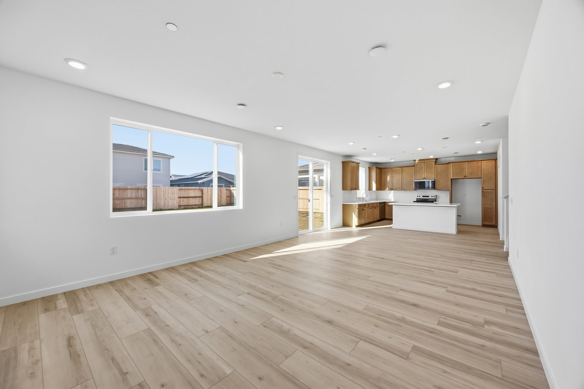 great room with light wood floors, white walls, large window looking out to backyard, and recessed ceiling lights