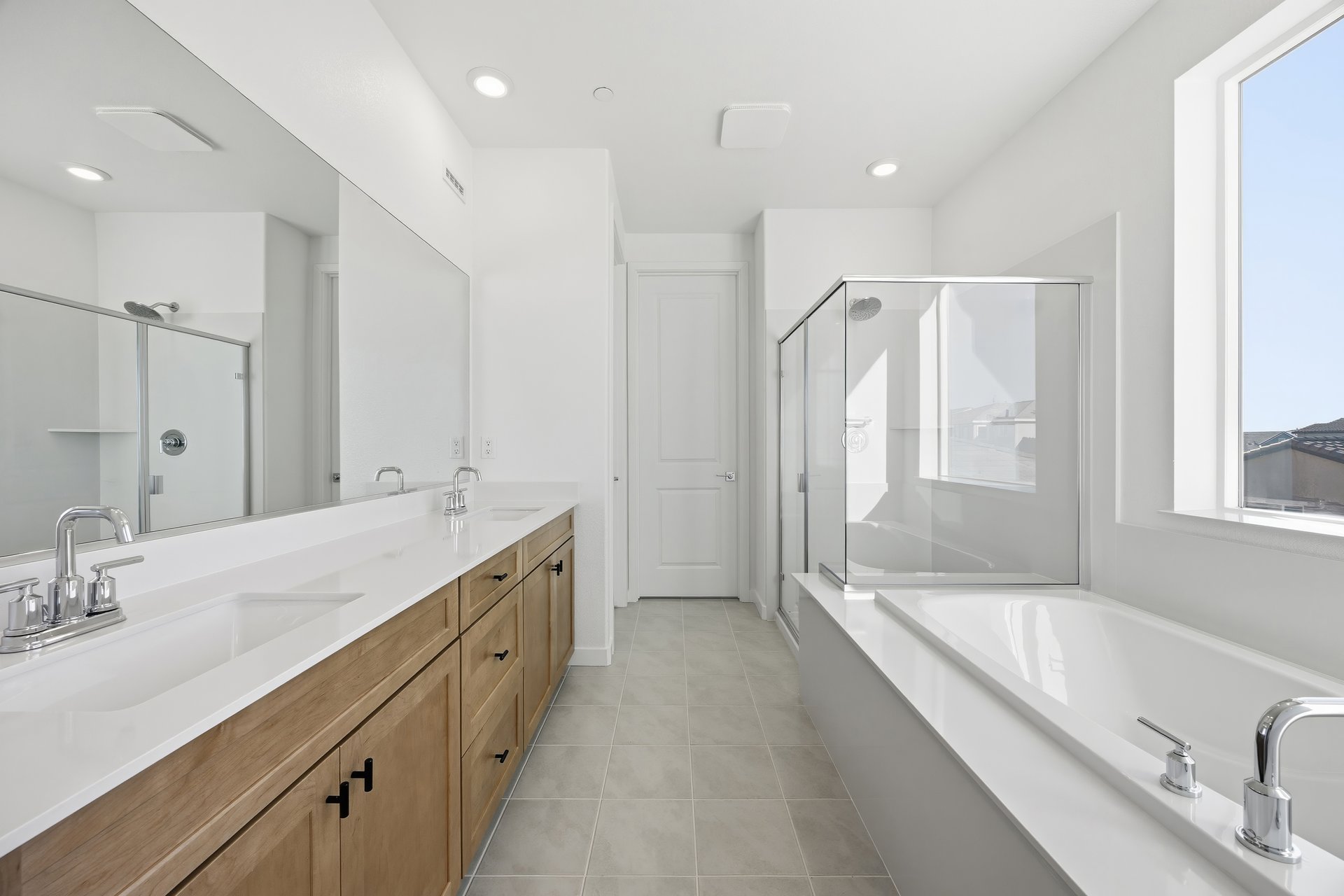 bathroom with light wood cabinets, white counters, two sinks, walk-in shower, and window above soaking tub