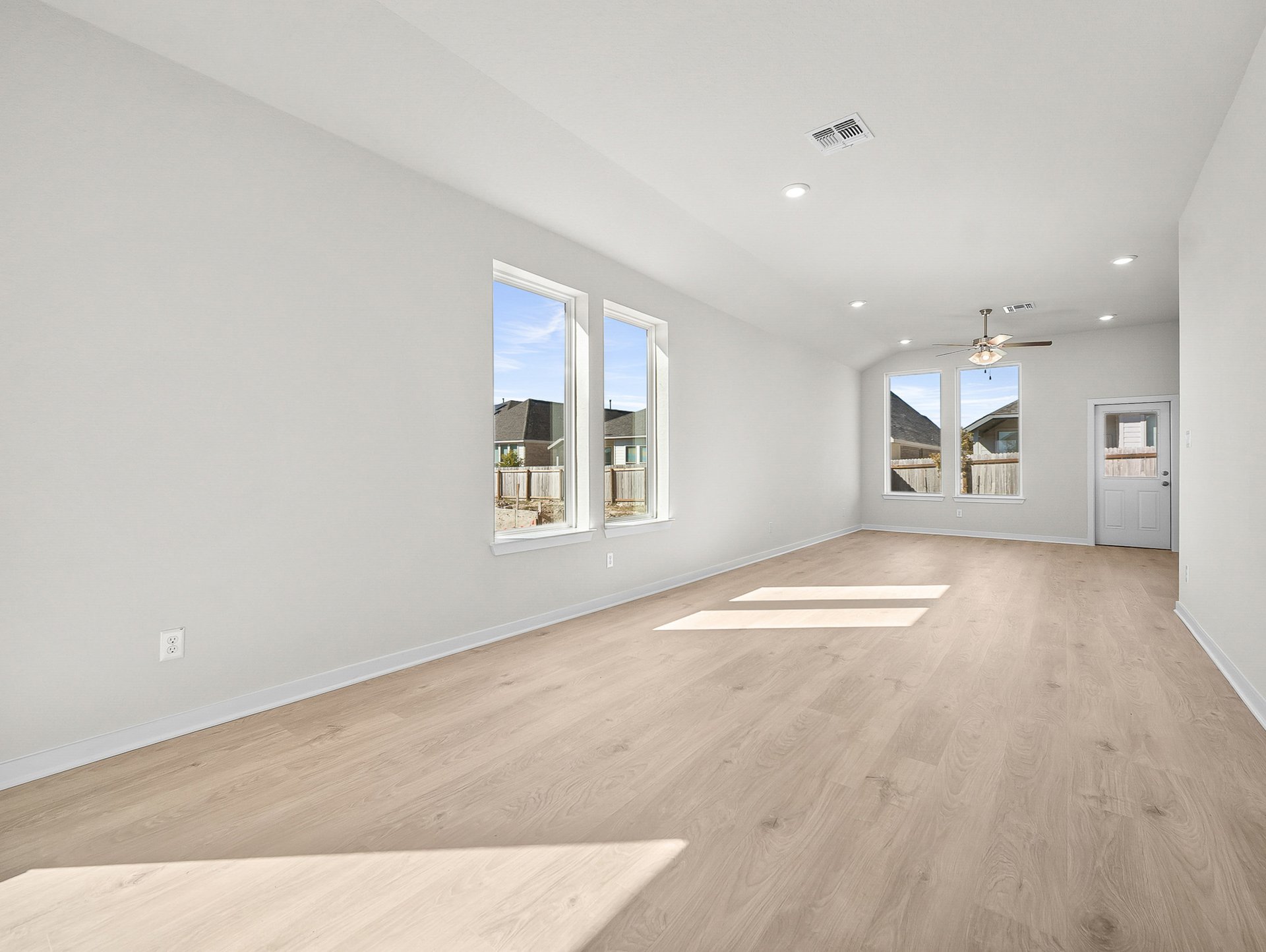 great room with brown flooring, windows & a ceiling fan