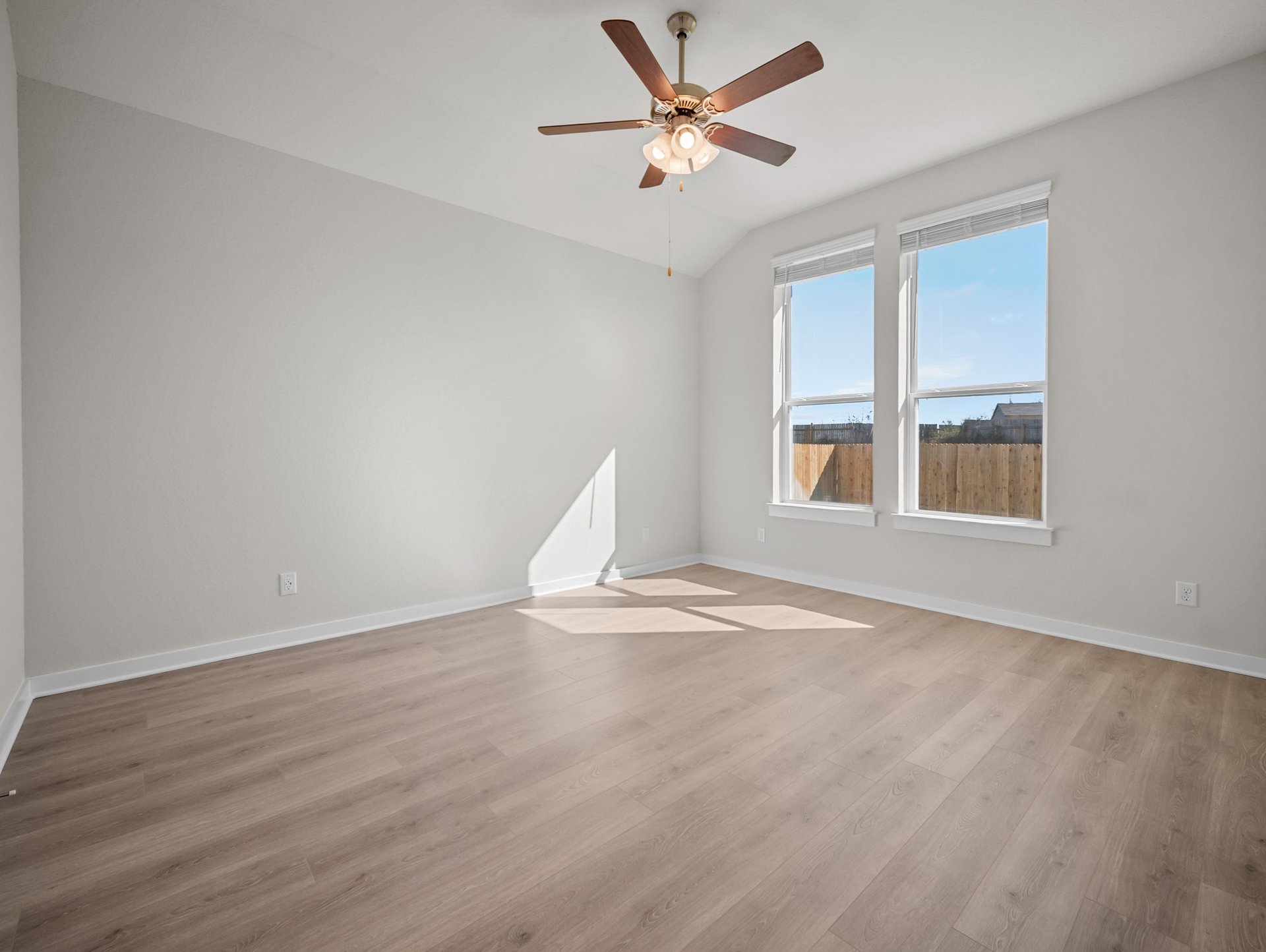 bedroom with brown flooring, ceiling fan & windows