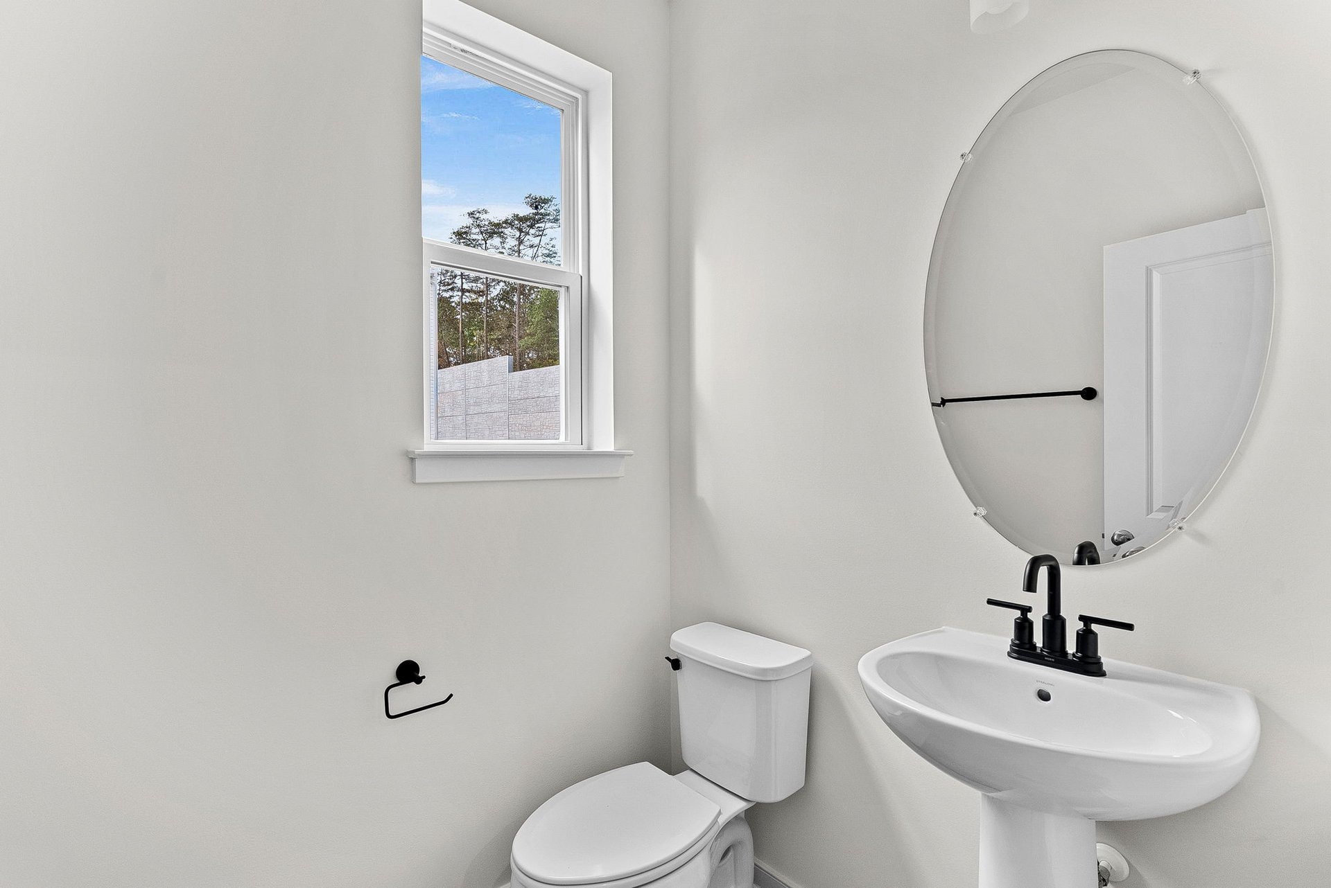 powder room with a window and oval mirror