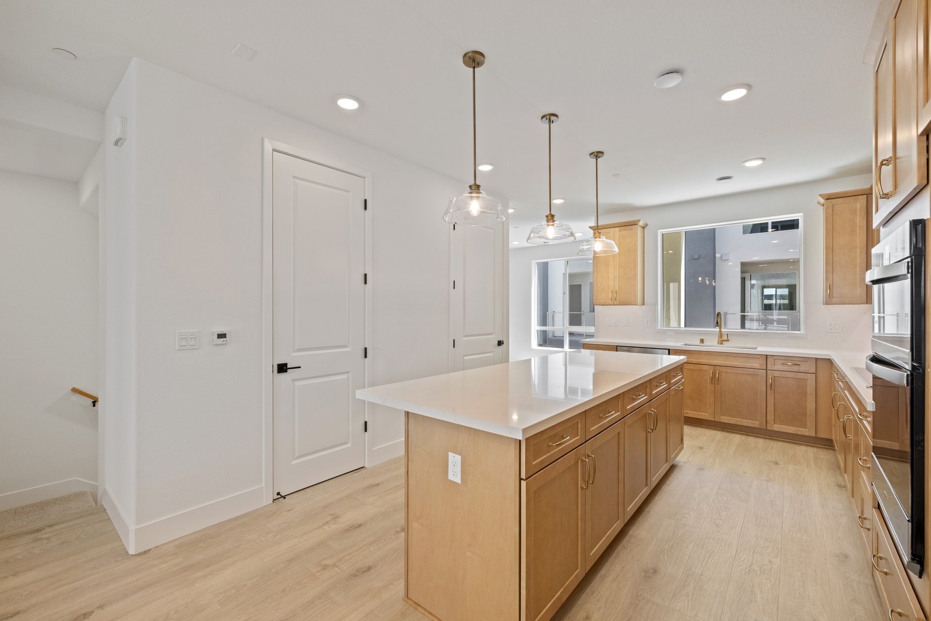 kitchen with brown cabinets, light wood floors, white quartz counters, island, and large window above sink