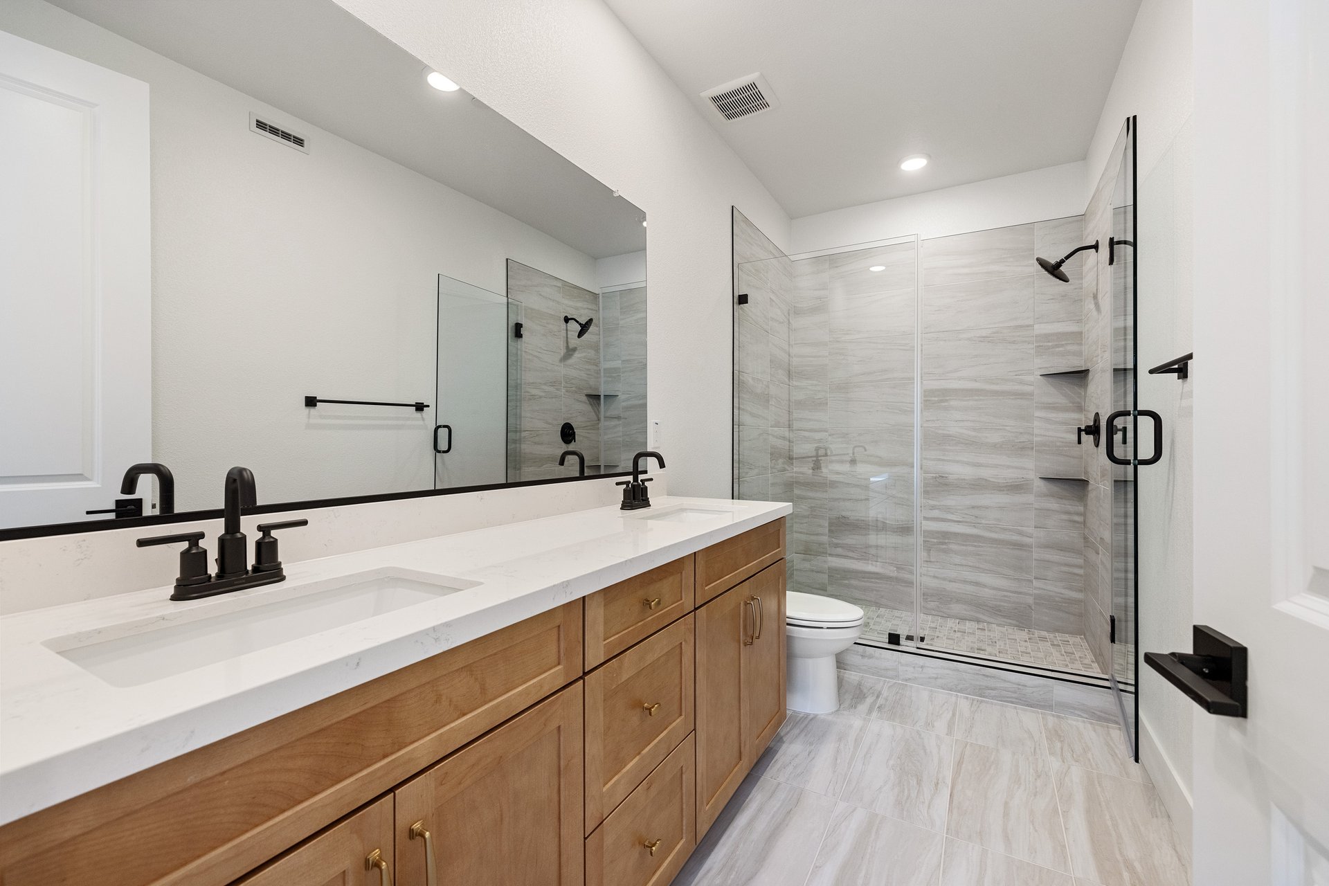 bathroom with gray and white patterned tile floors, wood cabinets, white counters, two sinks, and large walk-in shower
