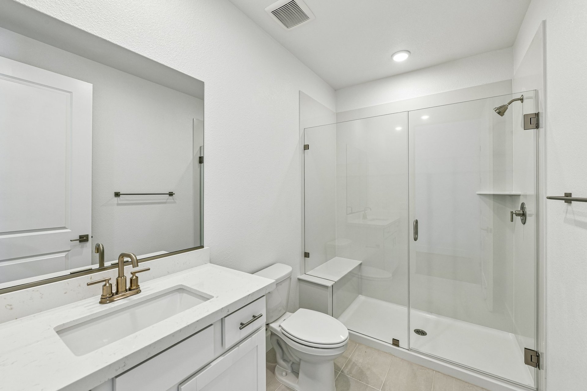 bathroom with white cabinets & counters, gold hardware & fixtures, and large walk-in shower with bench