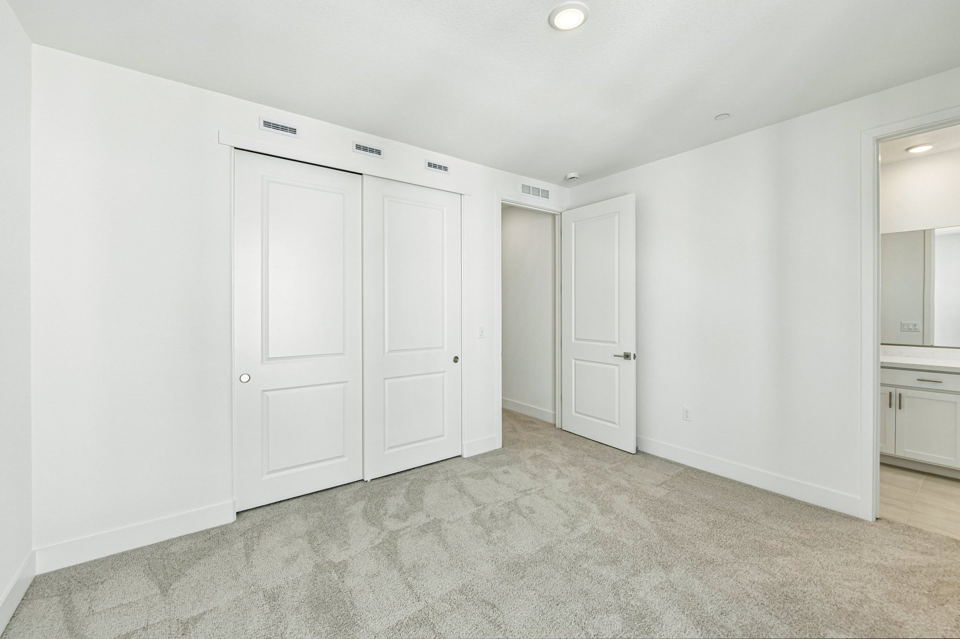 bedroom with tan carpet, white walls, and view of attached bathroom