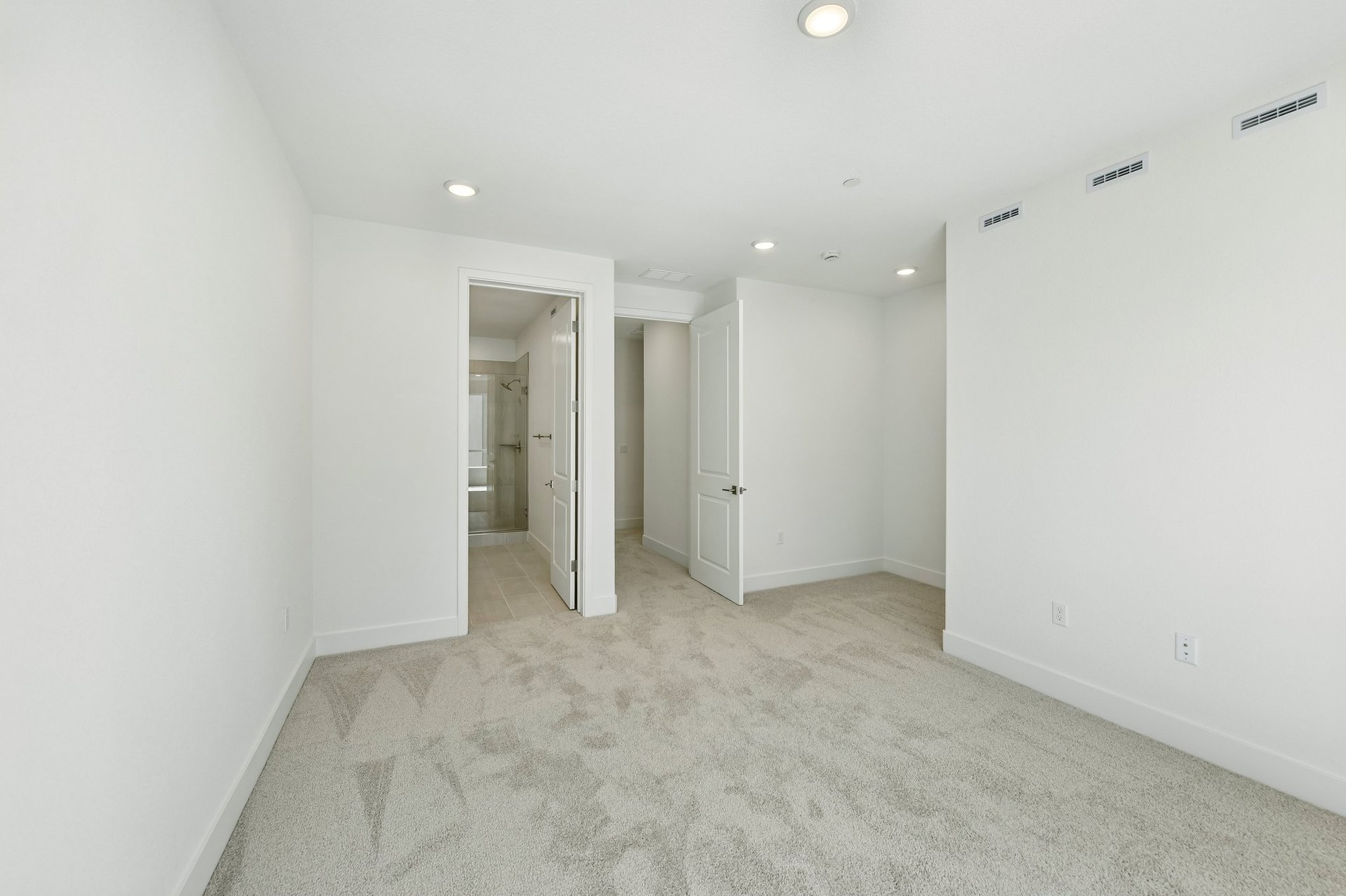 bedroom with white walls, tan carpet, and view of attached bathroom