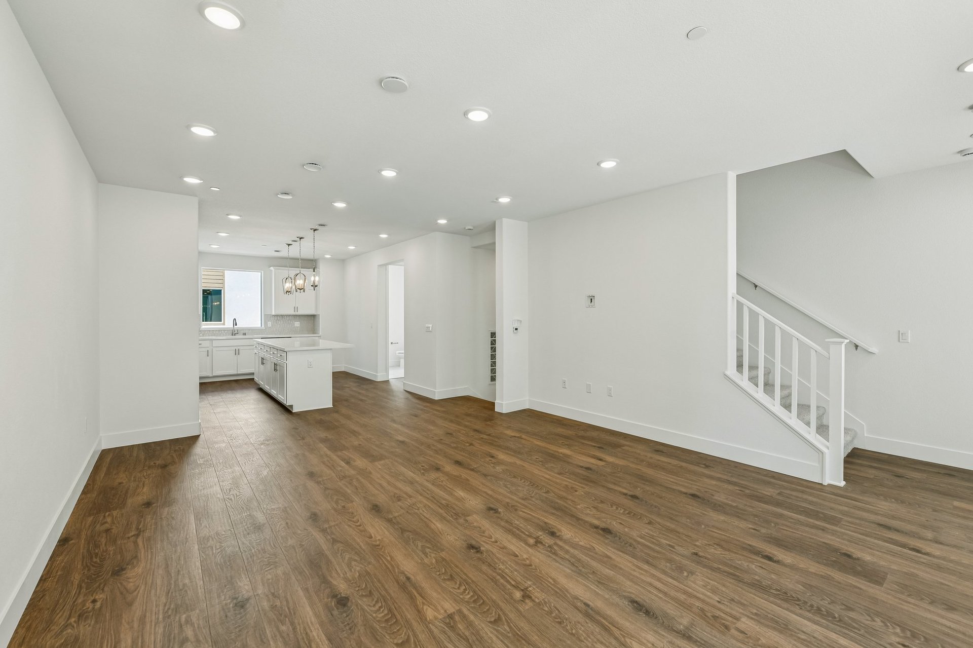 great room with wood floors, white walls, recessed ceiling lights, and view of kitchen with white cabinets