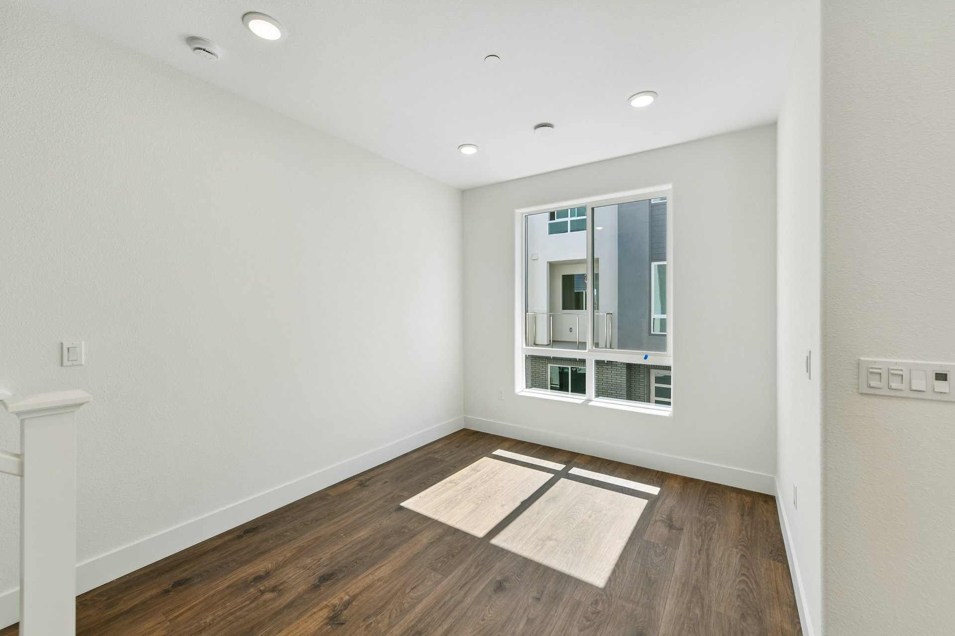 room with wood floors, white walls, recessed ceiling lights, and large window