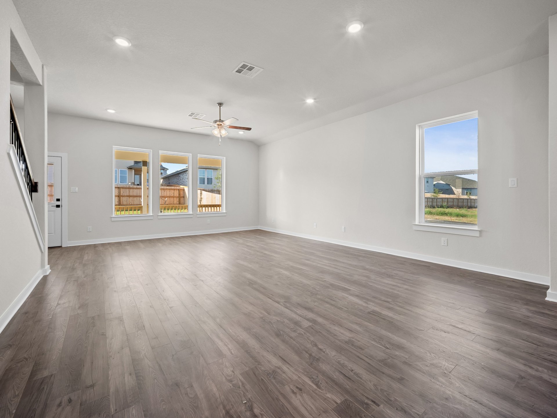 great room with brown flooring, ceiling fan & windows