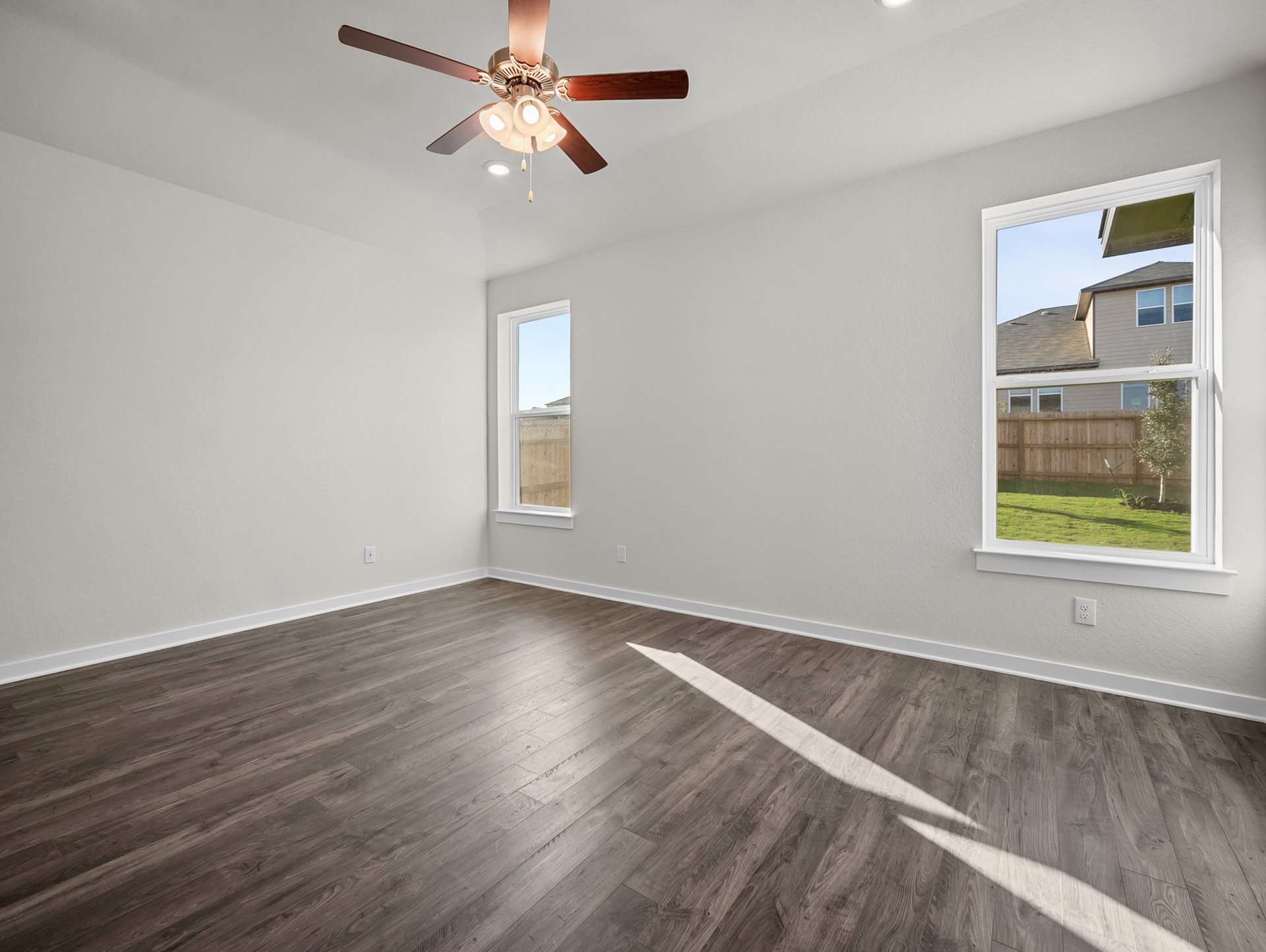 bedroom with brown flooring, windows & a ceiling fan