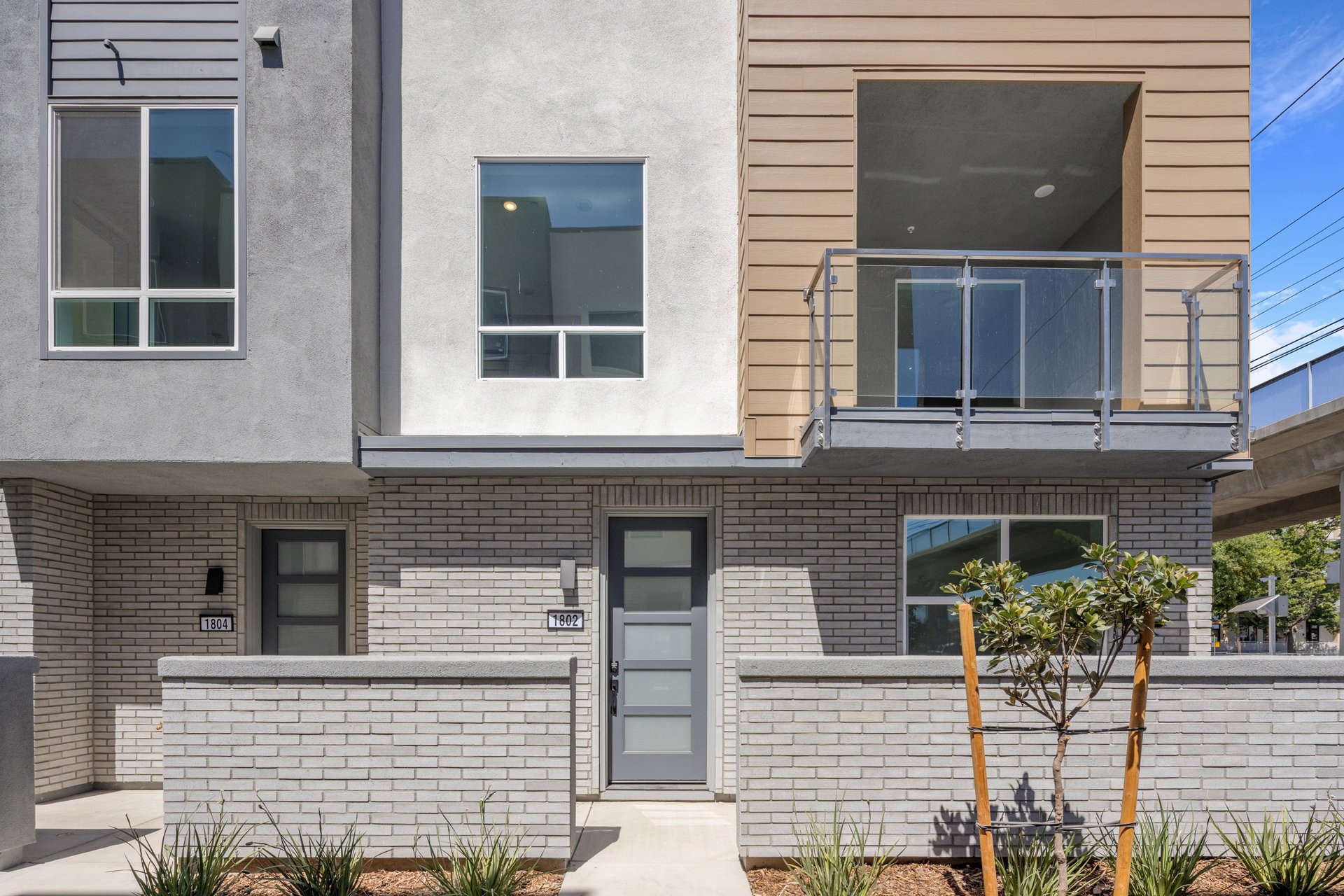 front exterior of brown and gray condo building with brick courtyards, black front doors, and glass enclosed balcony