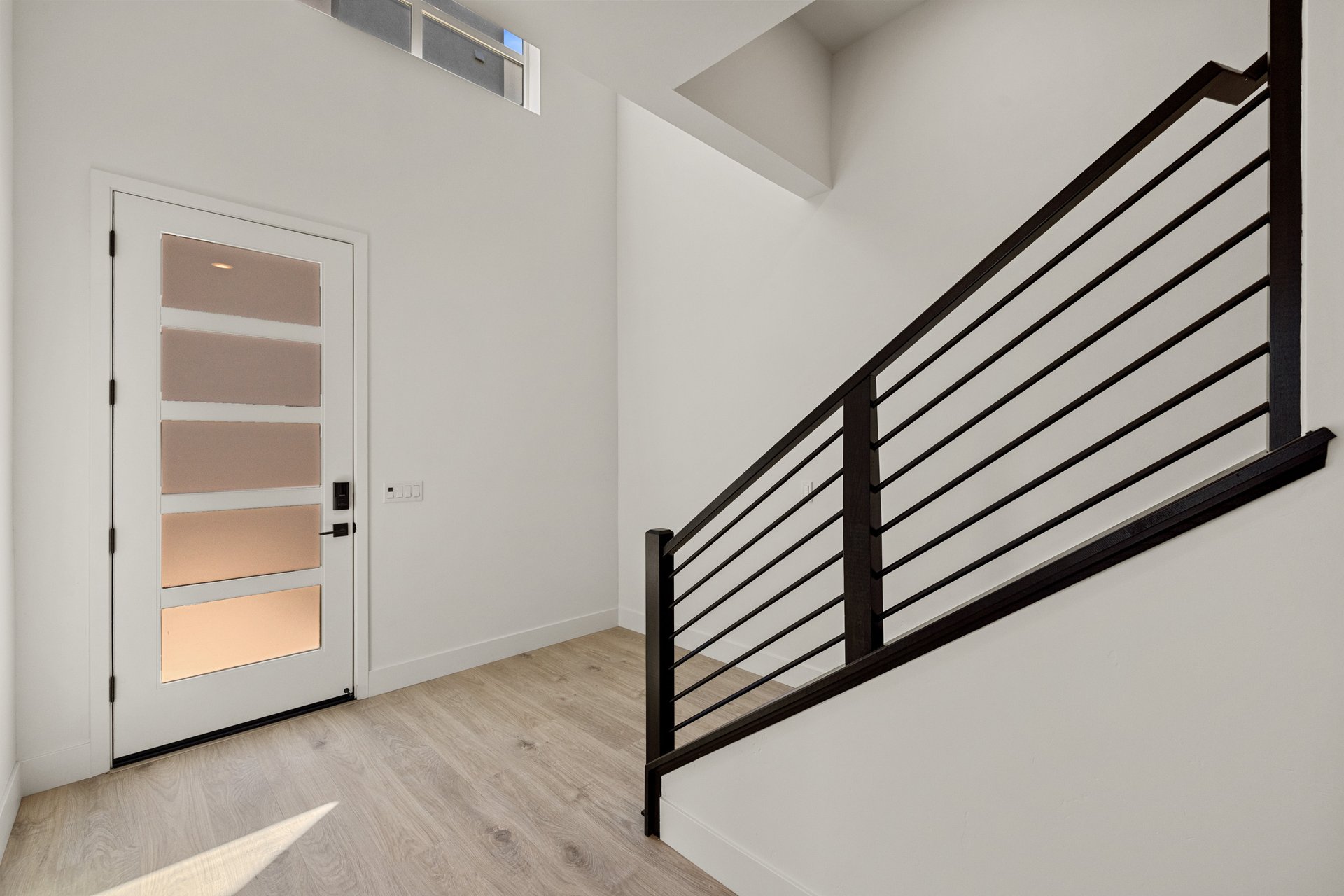 entry foyer with light wood floors, glass front door, and black modern stair rail