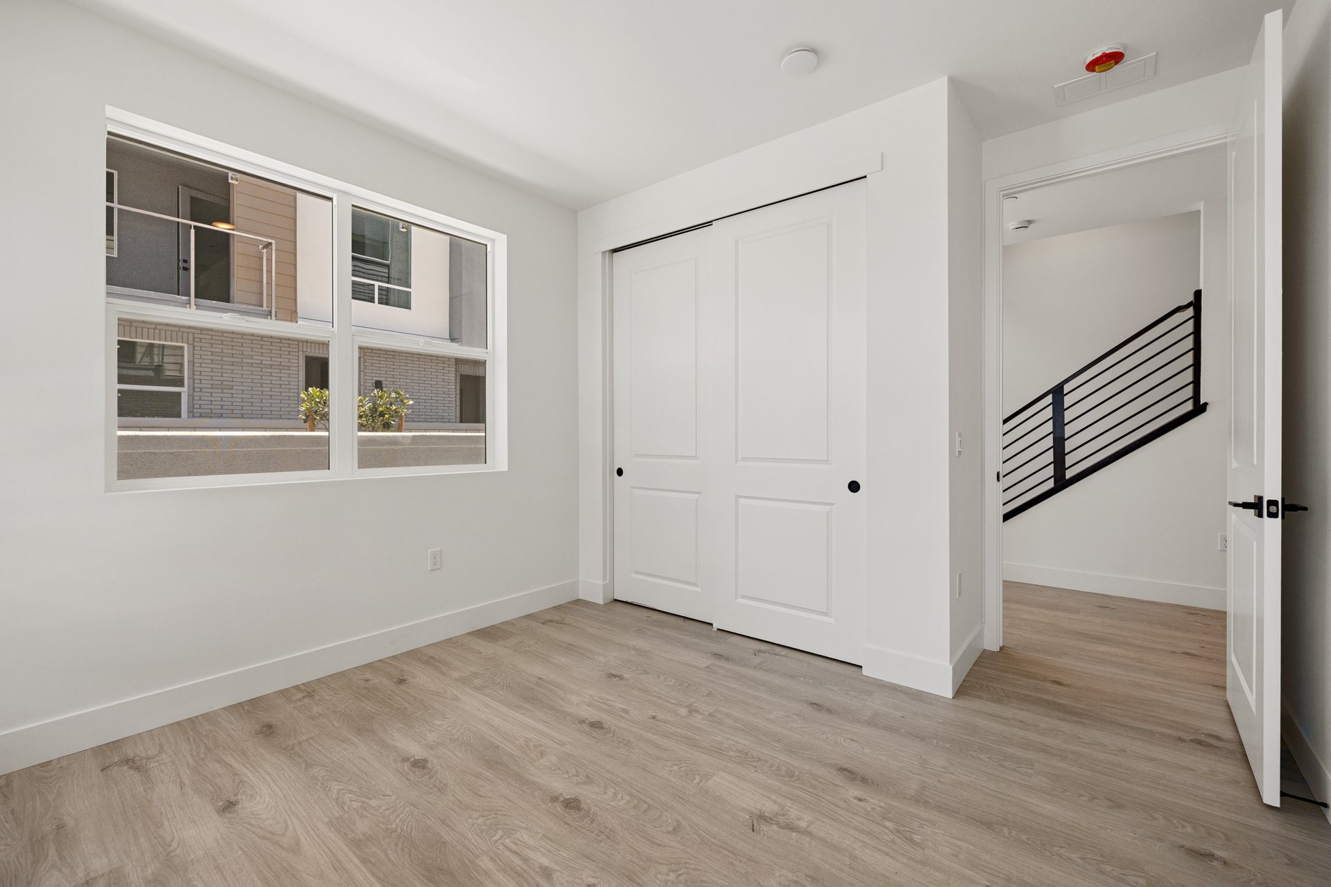 bedroom with window, light wood floors, closet, and view of black entry stair rail