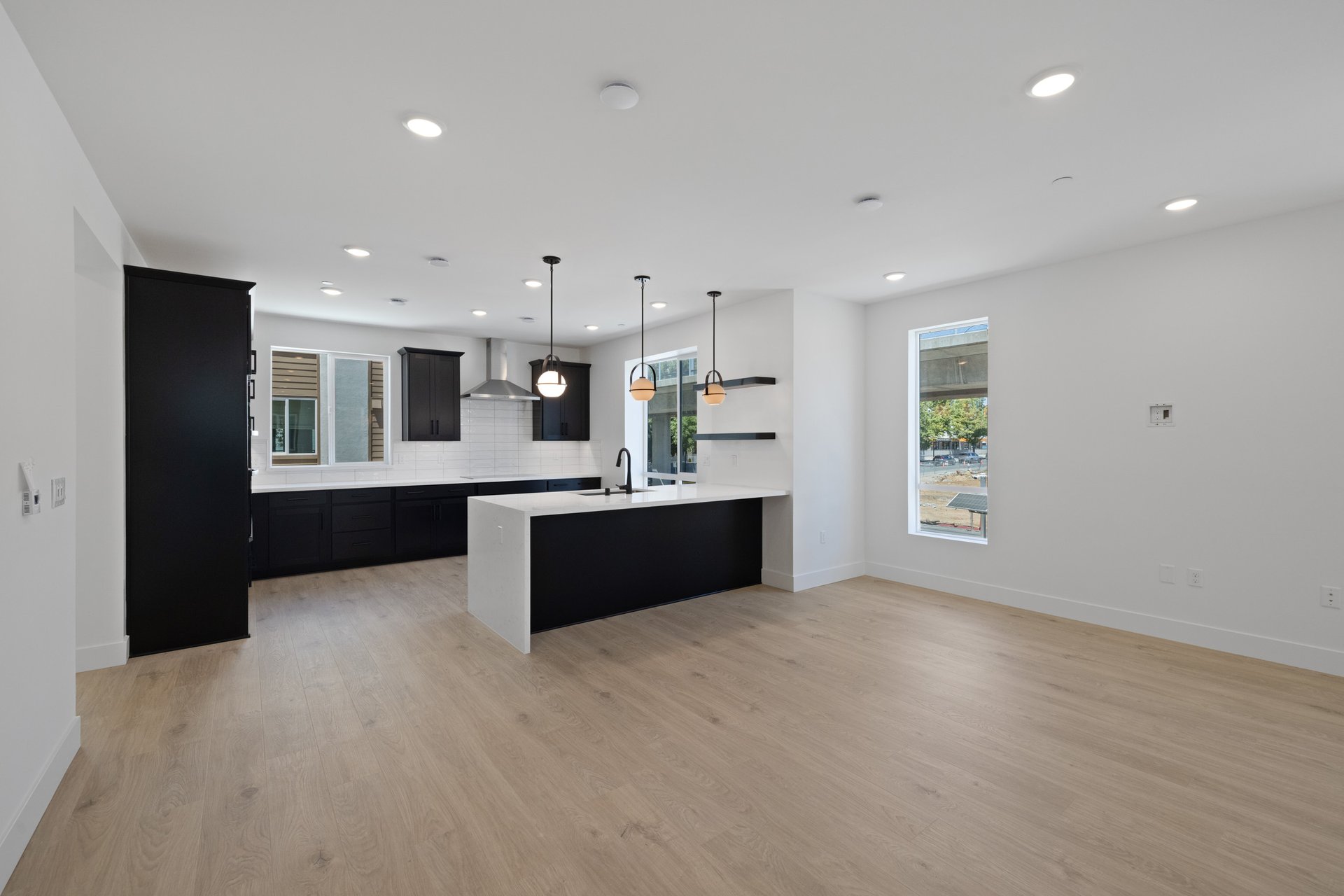 great room with white walls, light wood floors, and view of kitchen with black cabinets