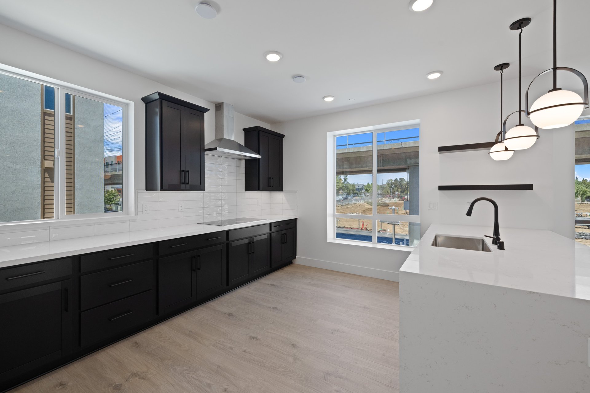 kitchen with light wood floors, black cabinets, white quartz counters, two windows, and sink in island