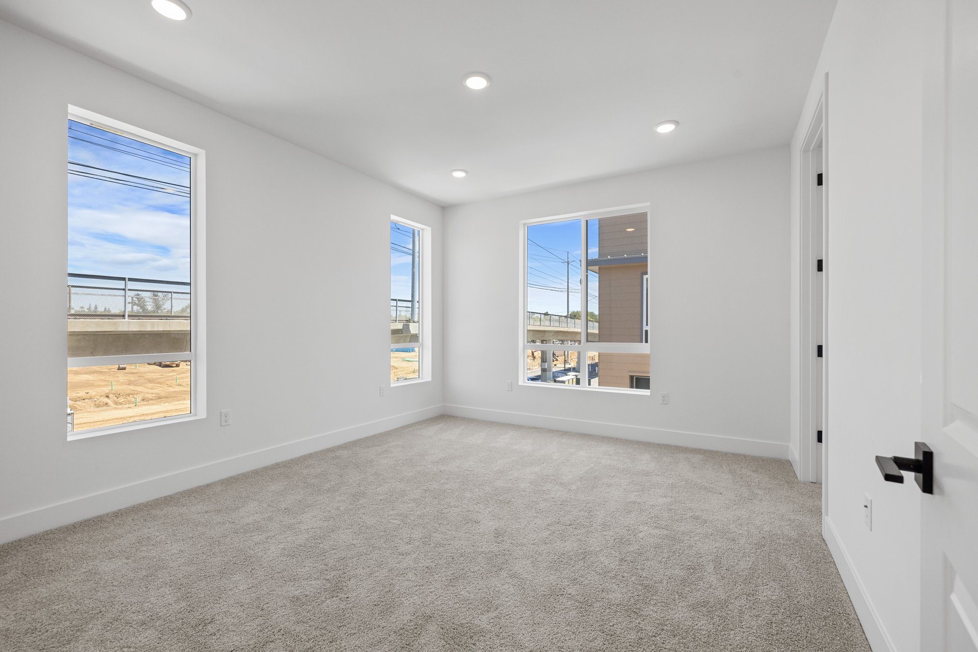 bedroom with three windows, tan carpet, and white walls