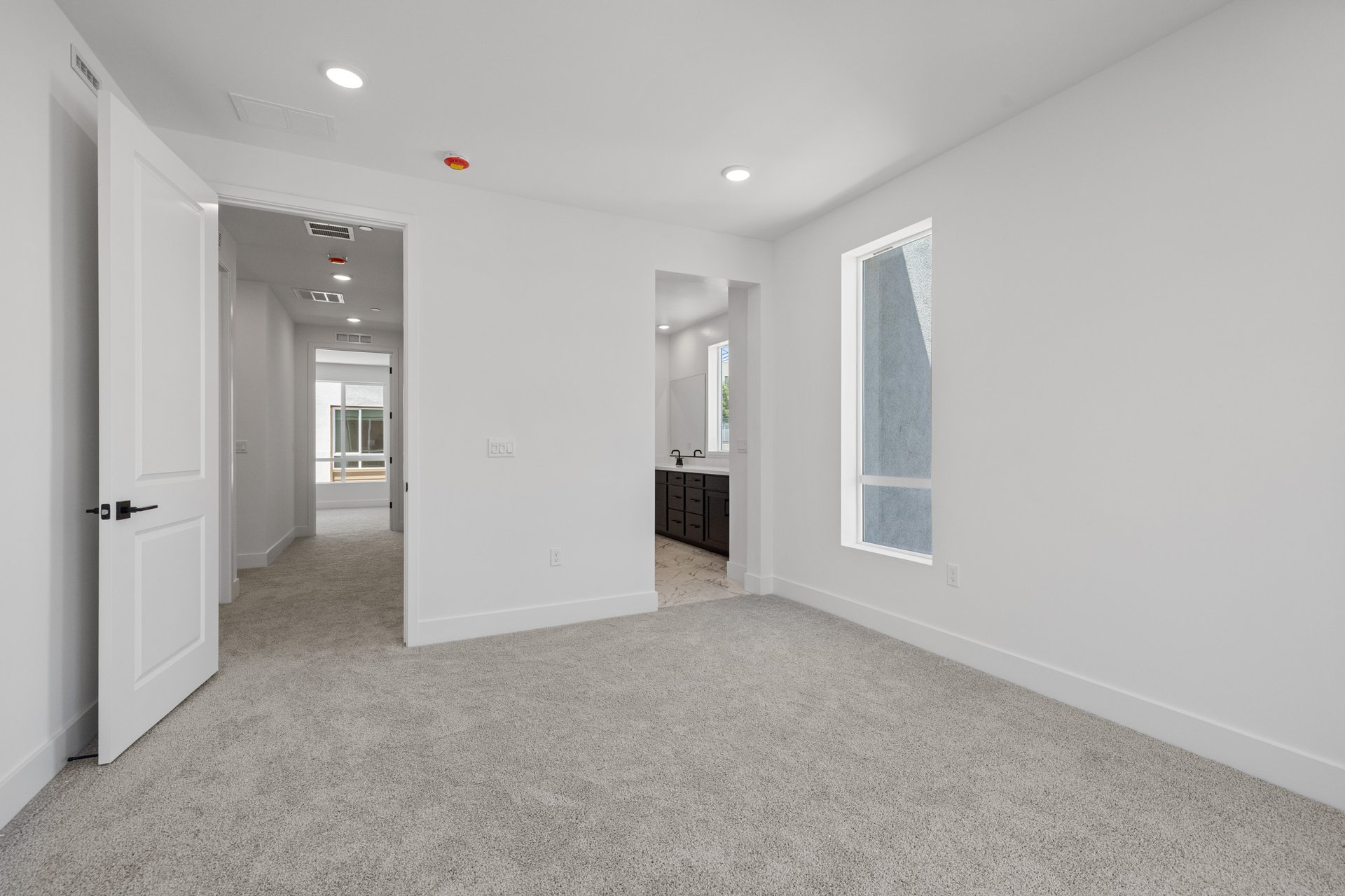 bedroom with tan carpet, white walls, window, and attached bathroom