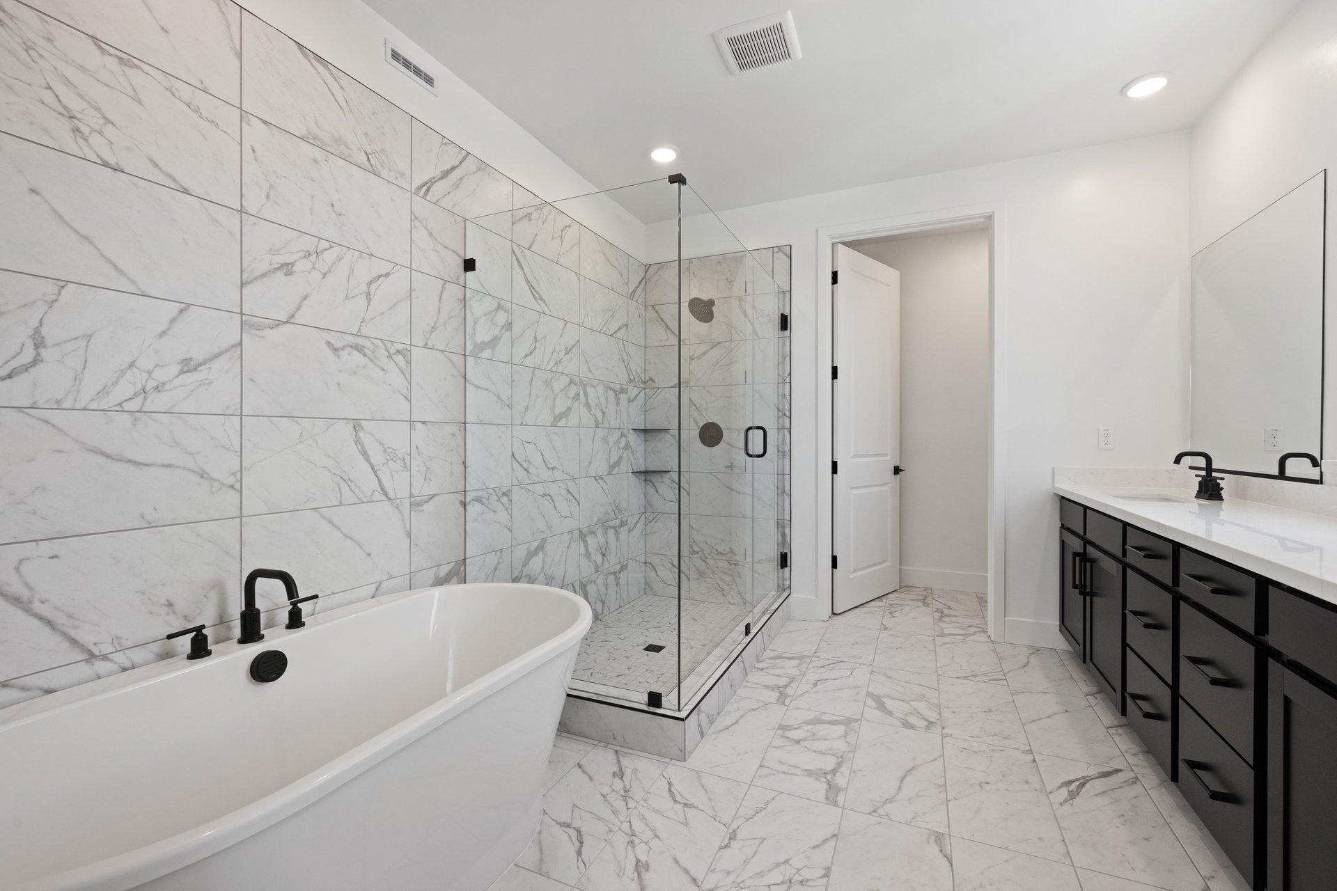 bathroom with white & gray tile on floors and wall, freestanding tub, walk-in shower, and black cabinets