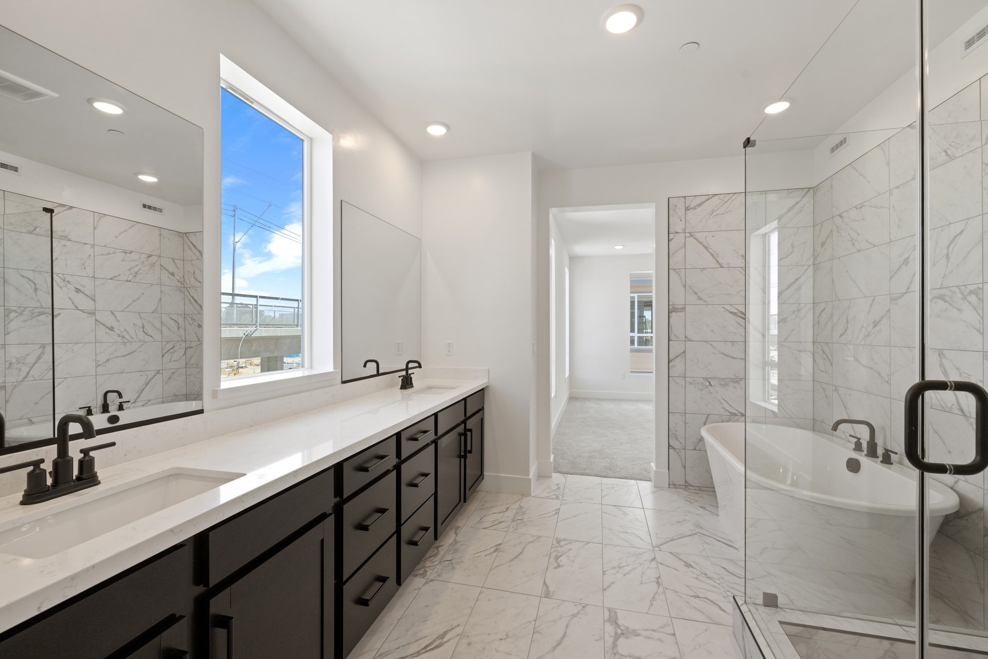 bathroom with black cabinets, white counters, two sinks, white & gray tile floor and wall, freestanding tub, and walk-in shower