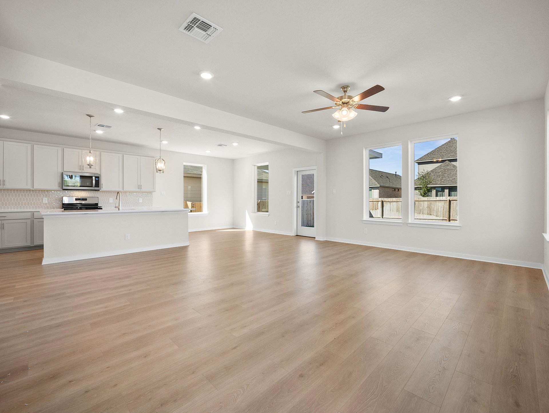 great room with brown flooring, ceiling fan & windows