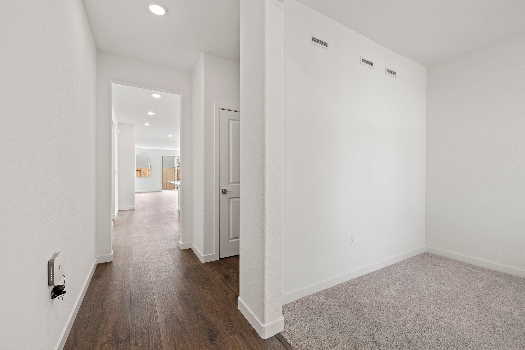 entry foyer with wood floors, white walls, and view of study with tan carpet