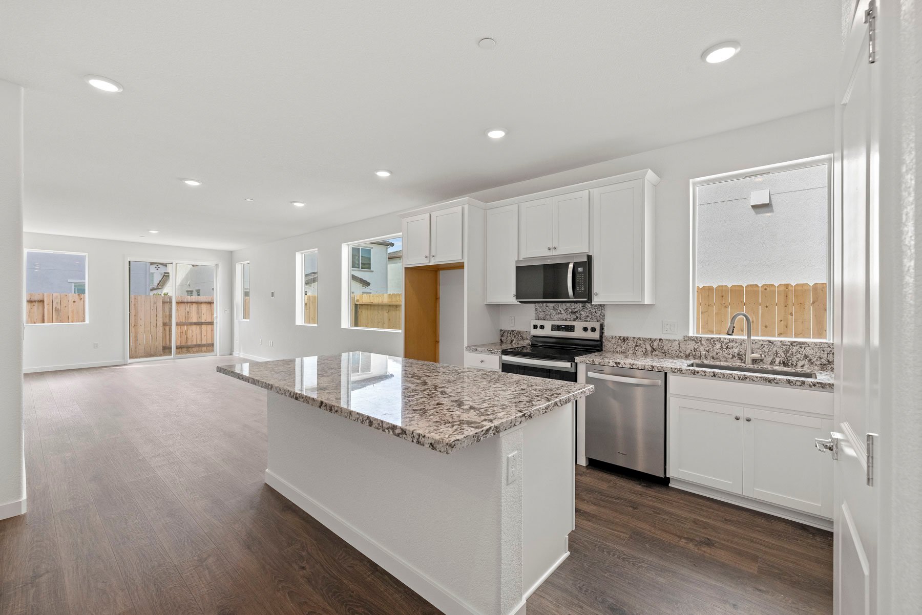 kitchen with white cabinets, granite counters, window, island, and wood floors