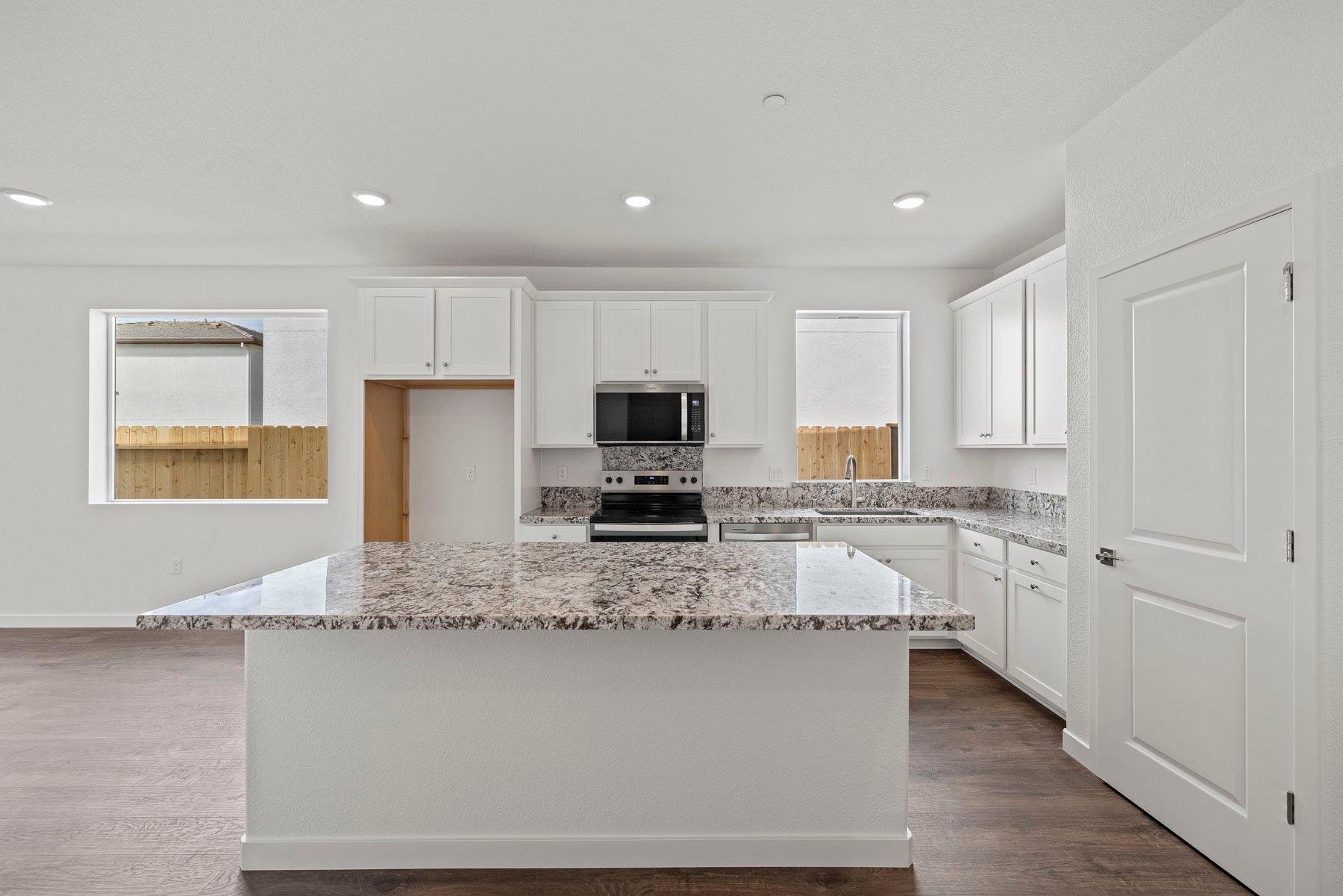 kitchen with white cabinets, granite counters, wood floors, island, and window over sink