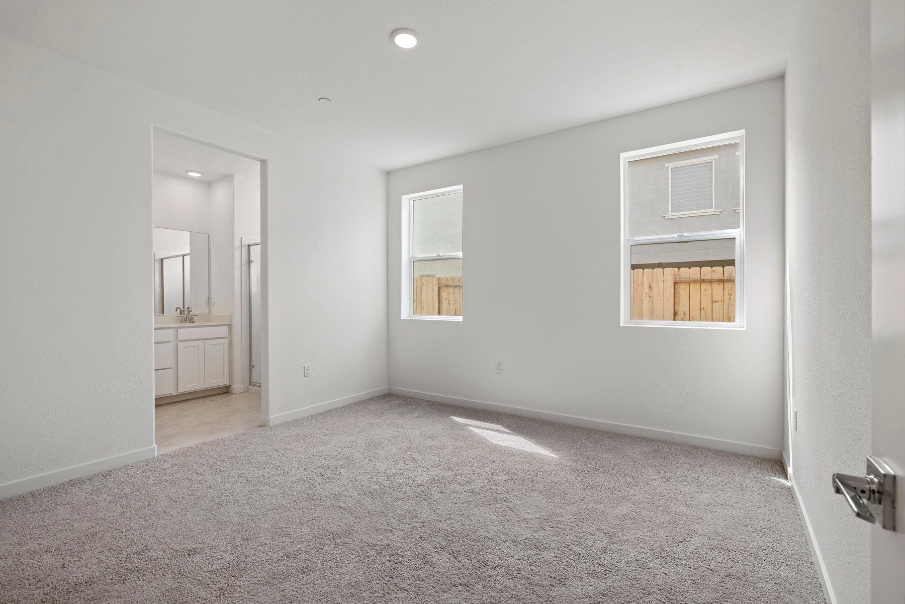 bedroom with tan carpet, white walls, two windows, and view of attached bathroom