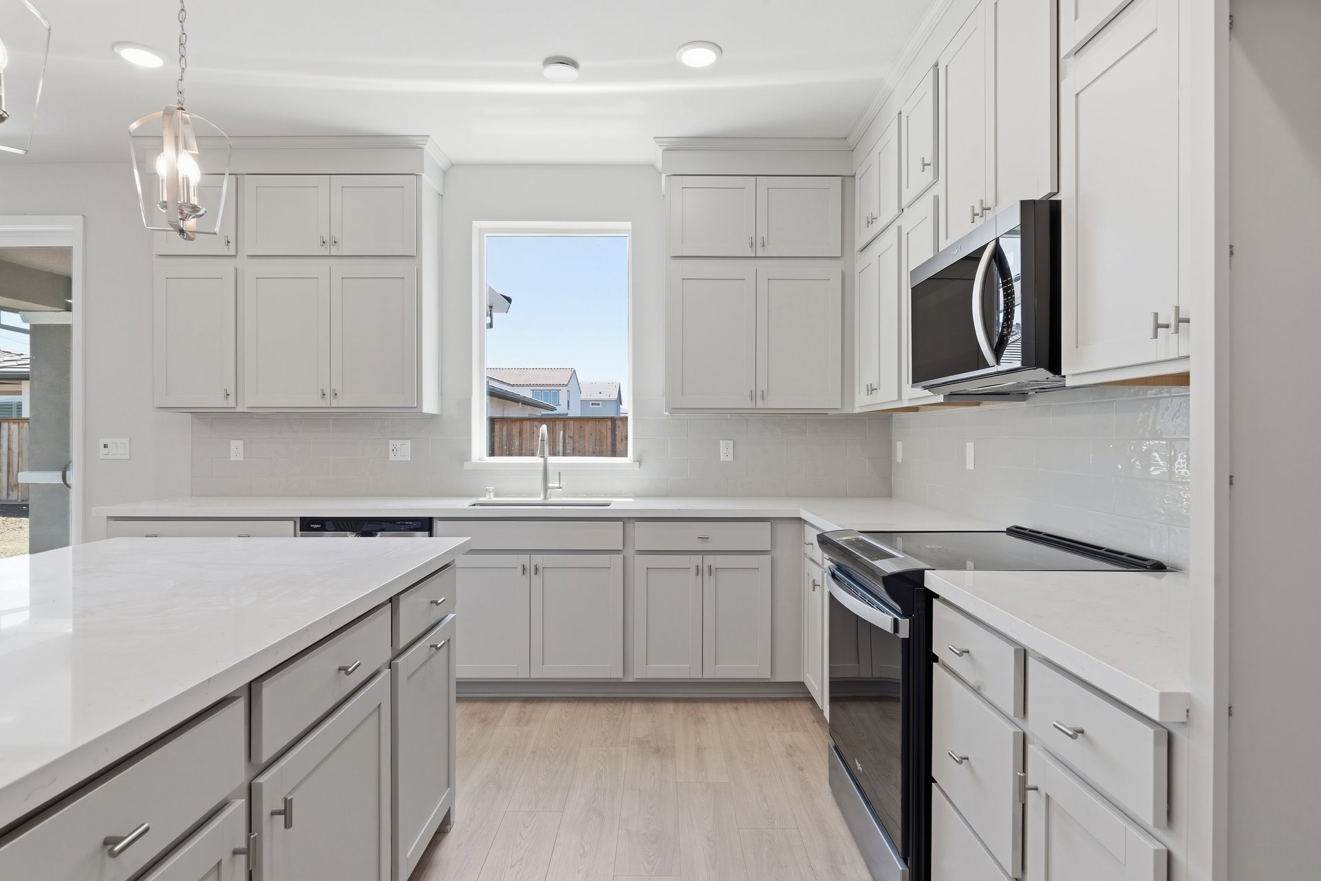 kitchen with light gray ceiling height cabinets, white counters, light wood floors, and window looking out to the backyard above sink