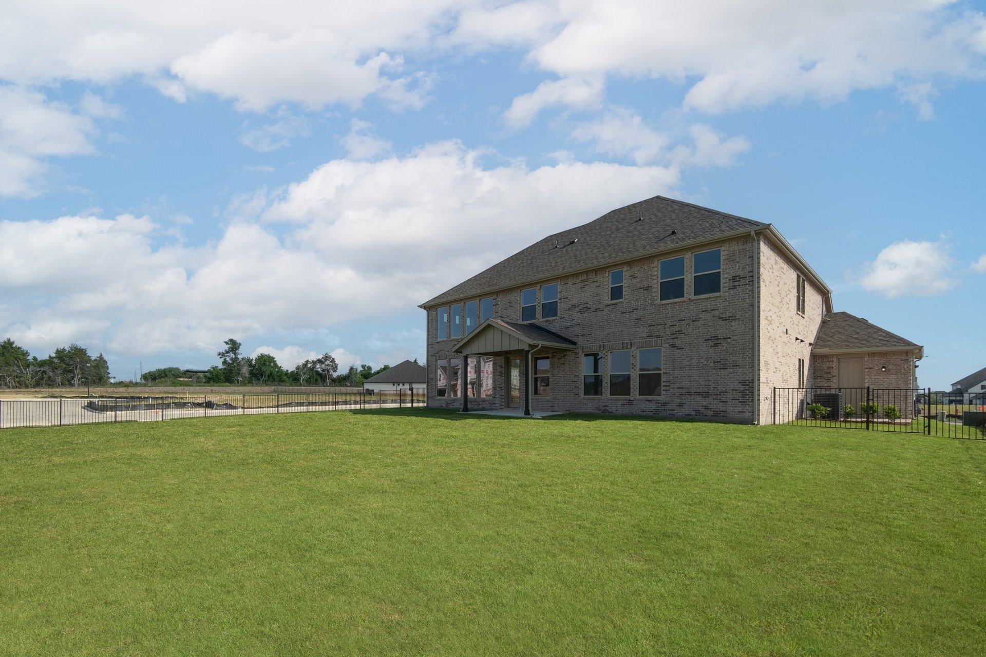 large backyard with wrought iron fence, grass, and covered patio