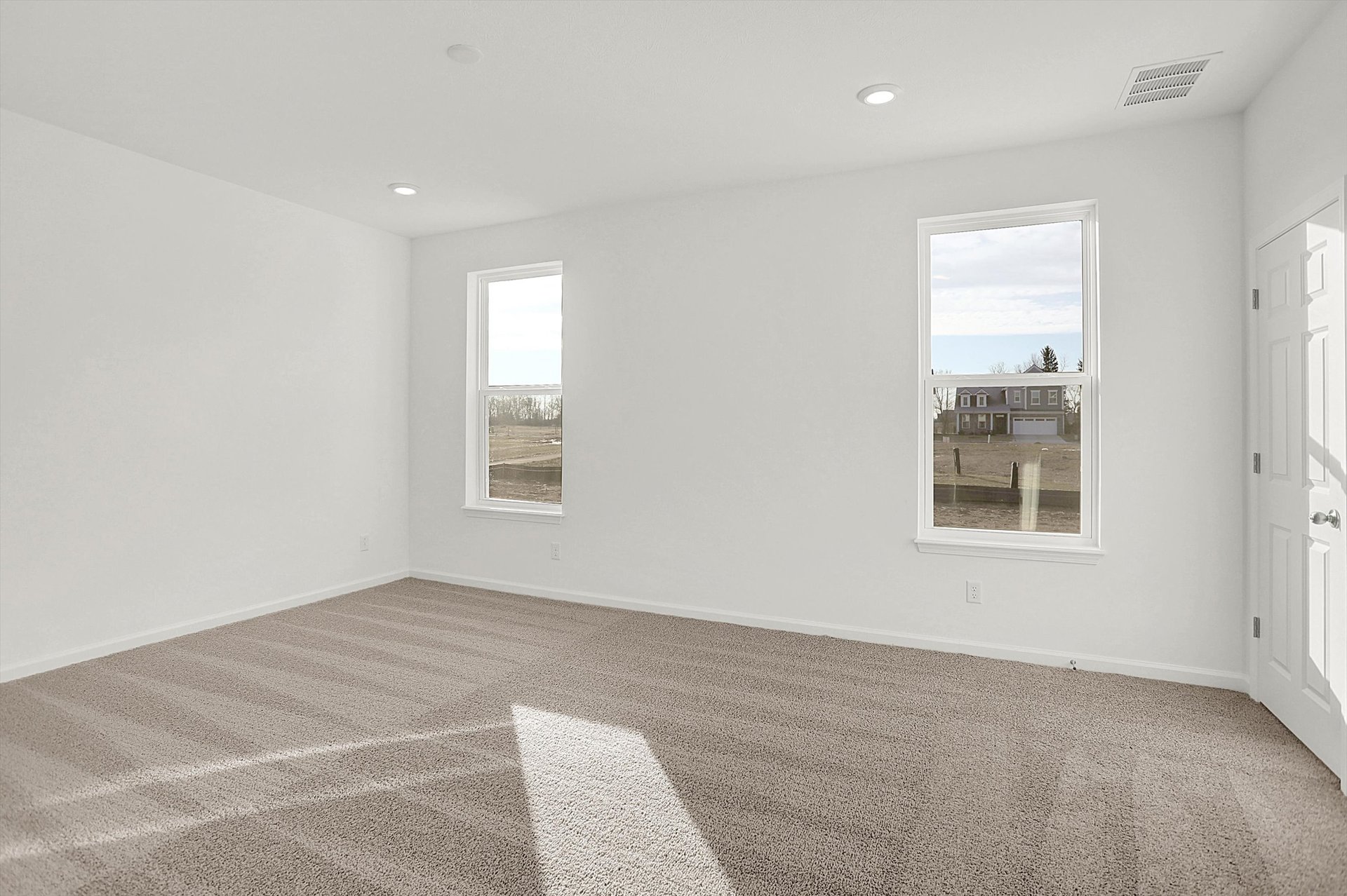 bedroom with tan carpet and windows letting in light