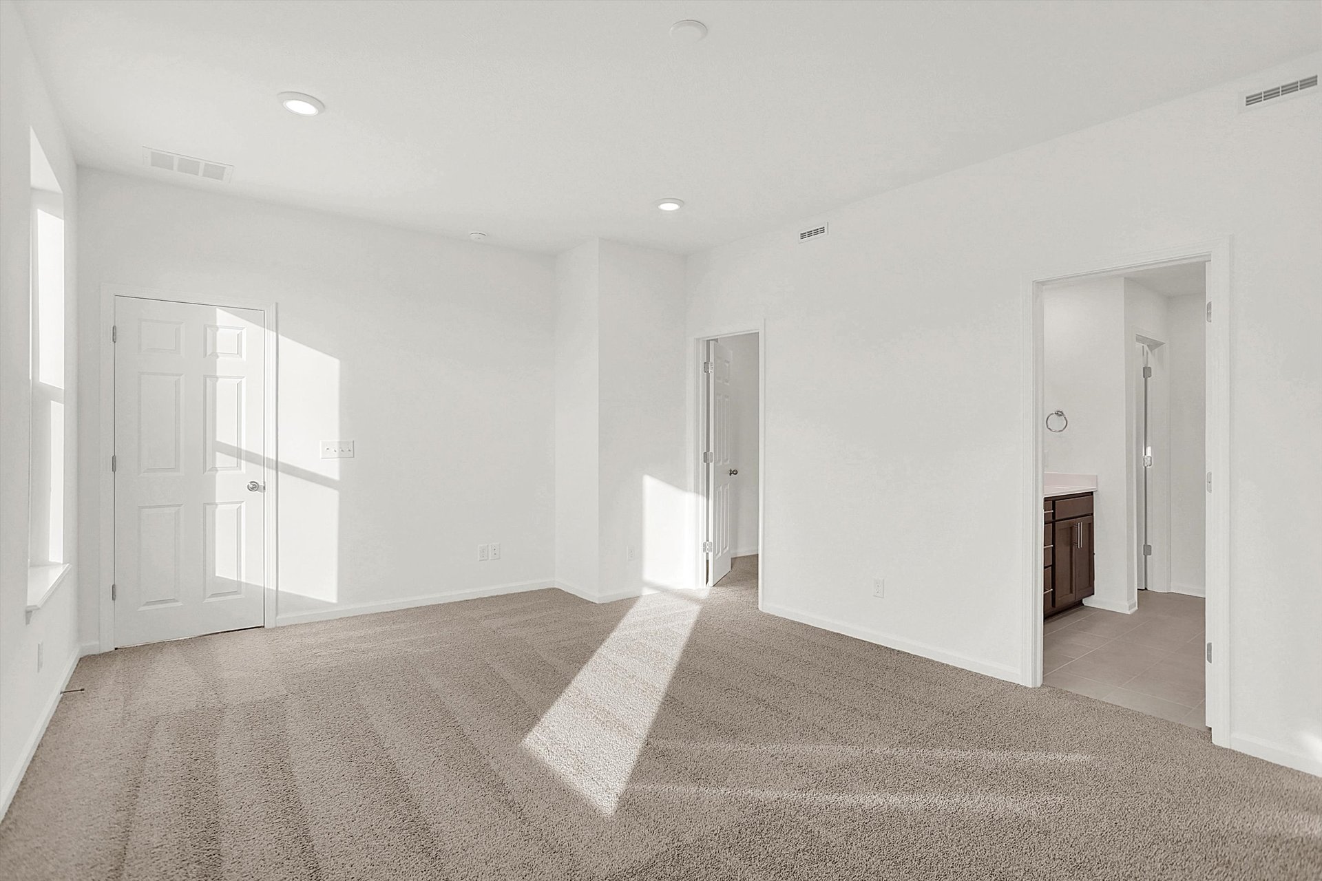 bedroom with tan carpet and doors leading to the closet and bathroom