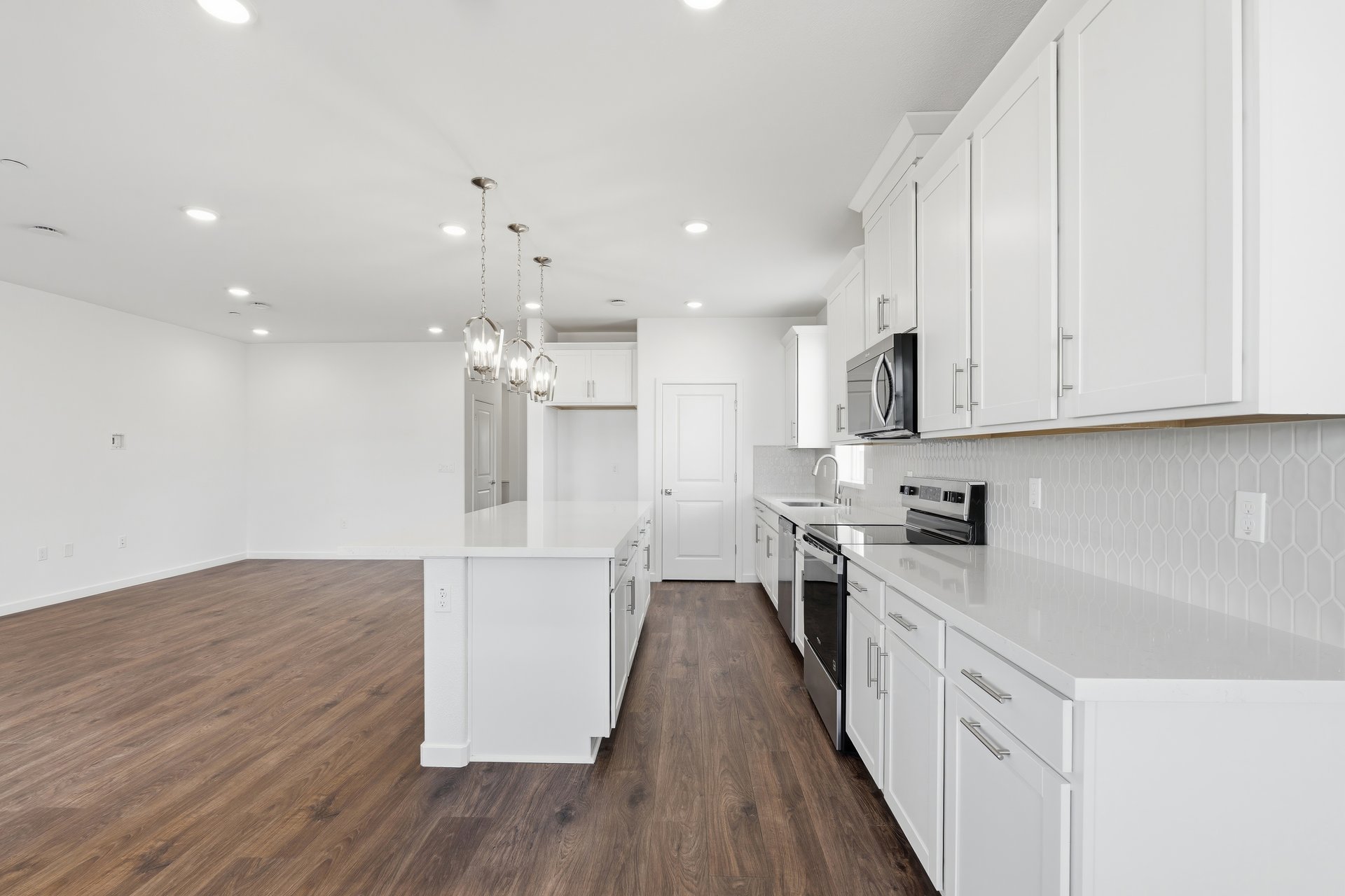 kitchen with wood floors, white cabinets, white counters, and three silver pendant lights above island