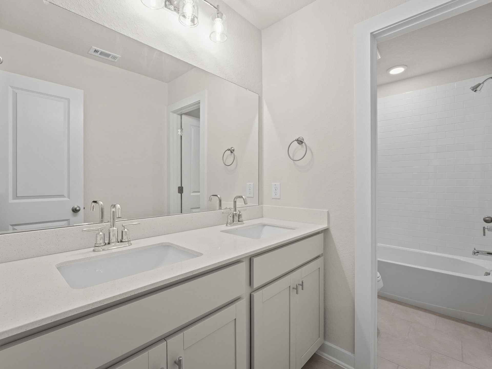 secondary bathroom with dual sinks, soaking tub and white cabinets