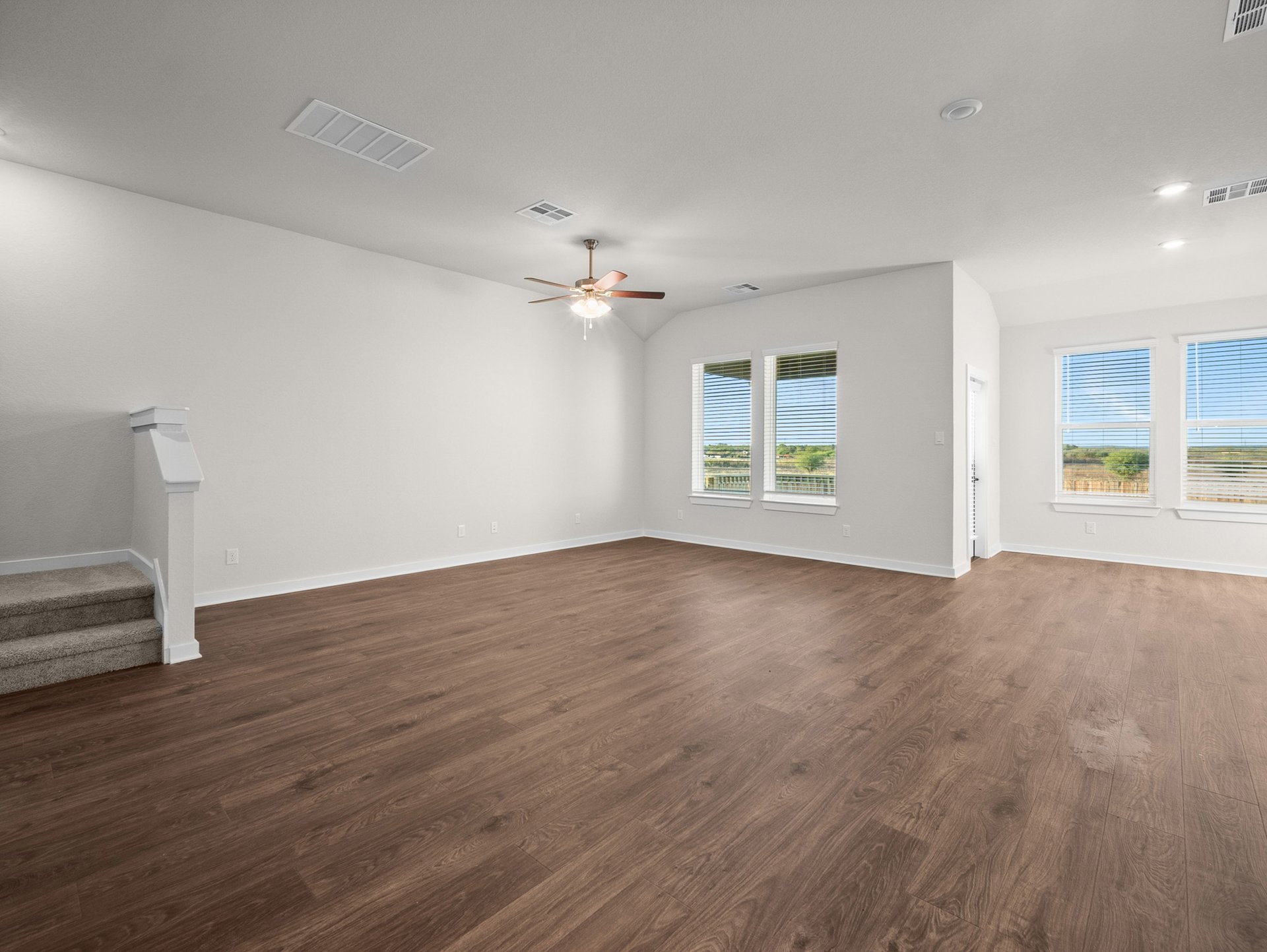 great room with brown flooring, windows & a ceiling fan
