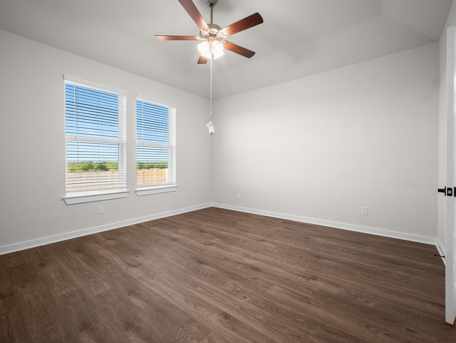 bedroom with brown flooring, windows & a ceiling fan