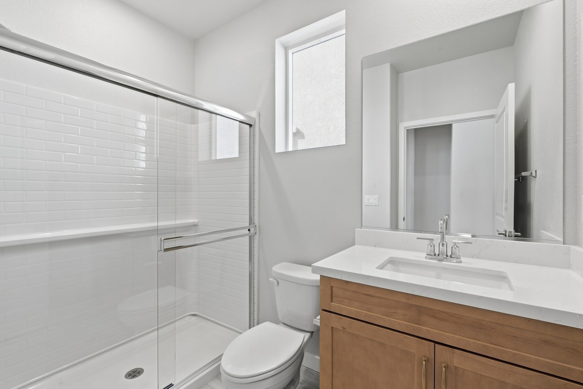 bathroom with light wood cabinets, white counter, walk-in shower, and window above toilet