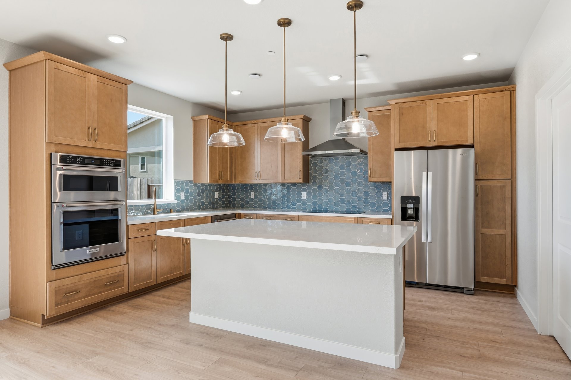 kitchen with light wood cabinets, white counters, blue tile backsplash, island, and window above sink
