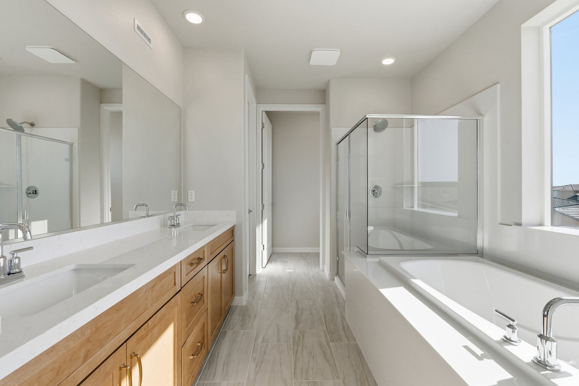 bathroom with light wood cabinets, white counters, two sinks, walk-in shower, and window above tub